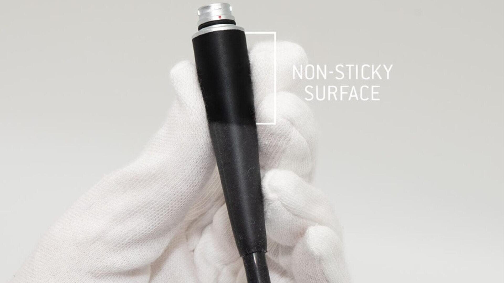 A hand in a white glove holds a black cylindrical object labeled NON-STICKY SURFACE against a light gray background.