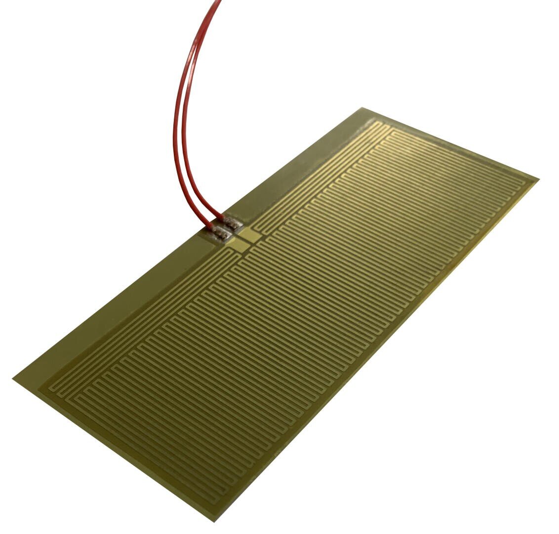 A rectangular flexible heating pad with a grid of thin parallel lines, connected to two red wires at one end. The pad is golden-yellow in color and slightly elevated from the surface.
