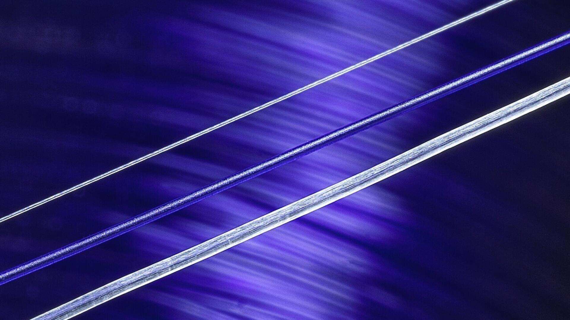 Close-up image of two thin, parallel wires or fibers against a blurred, purple and blue background with streaks of light.