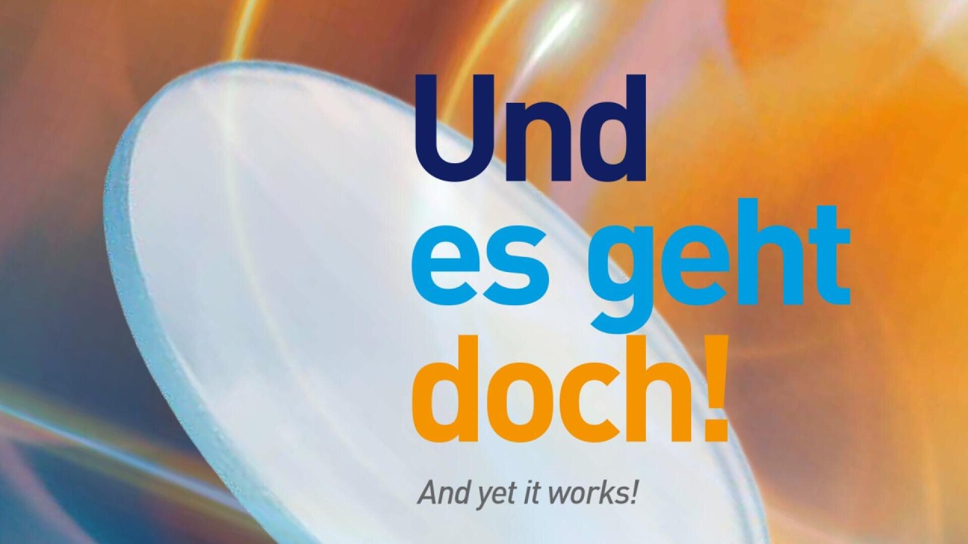 A blurred, colorful background with the German text Und es geht doch! in blue and orange, and the English translation And yet it works! below in gray font. A circular, translucent shape is on the left.