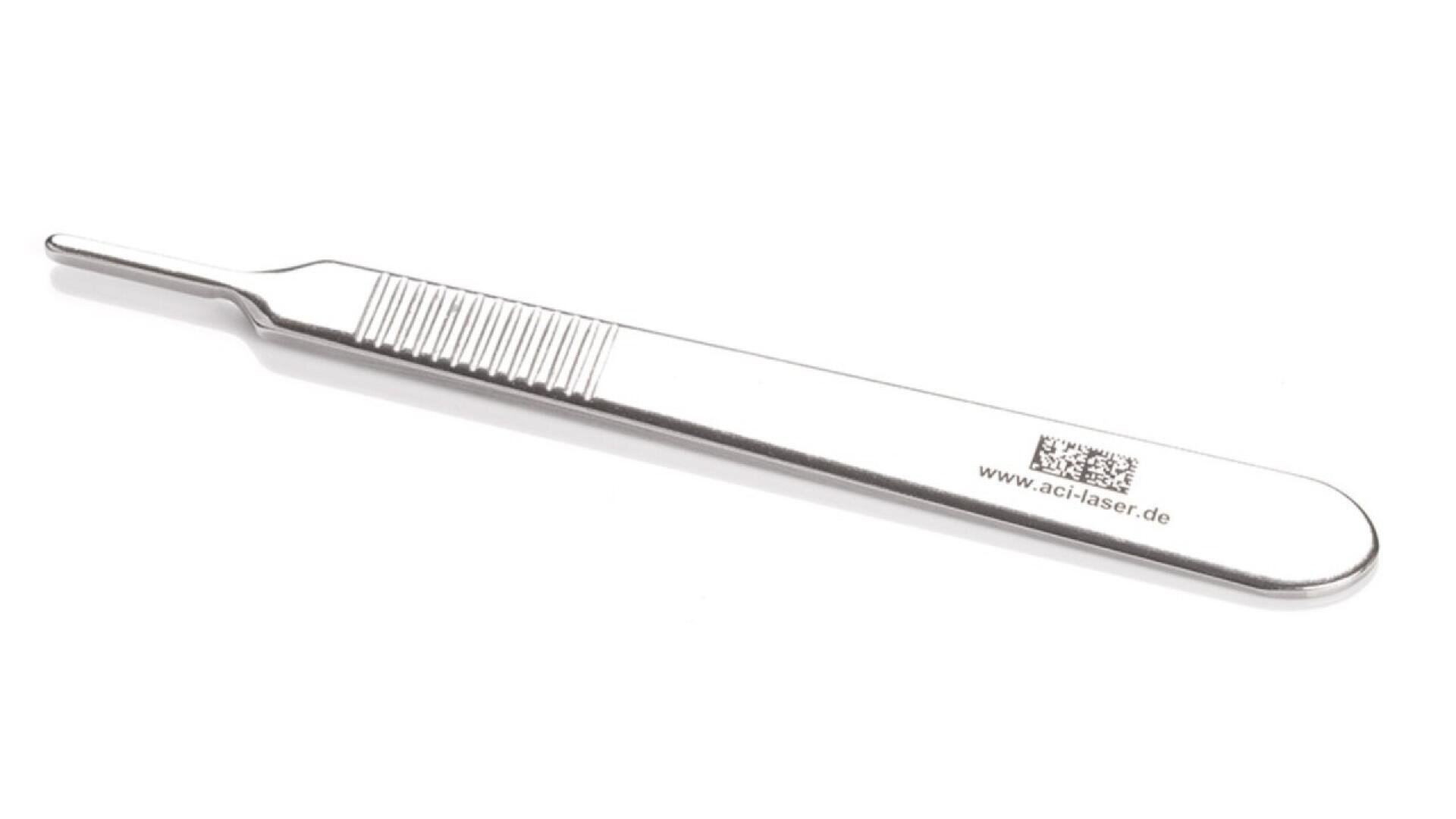 A stainless steel surgical scalpel handle with a flat, textured grip and a pointed tip, shown on a white background. The handle has engraved text and a website address.