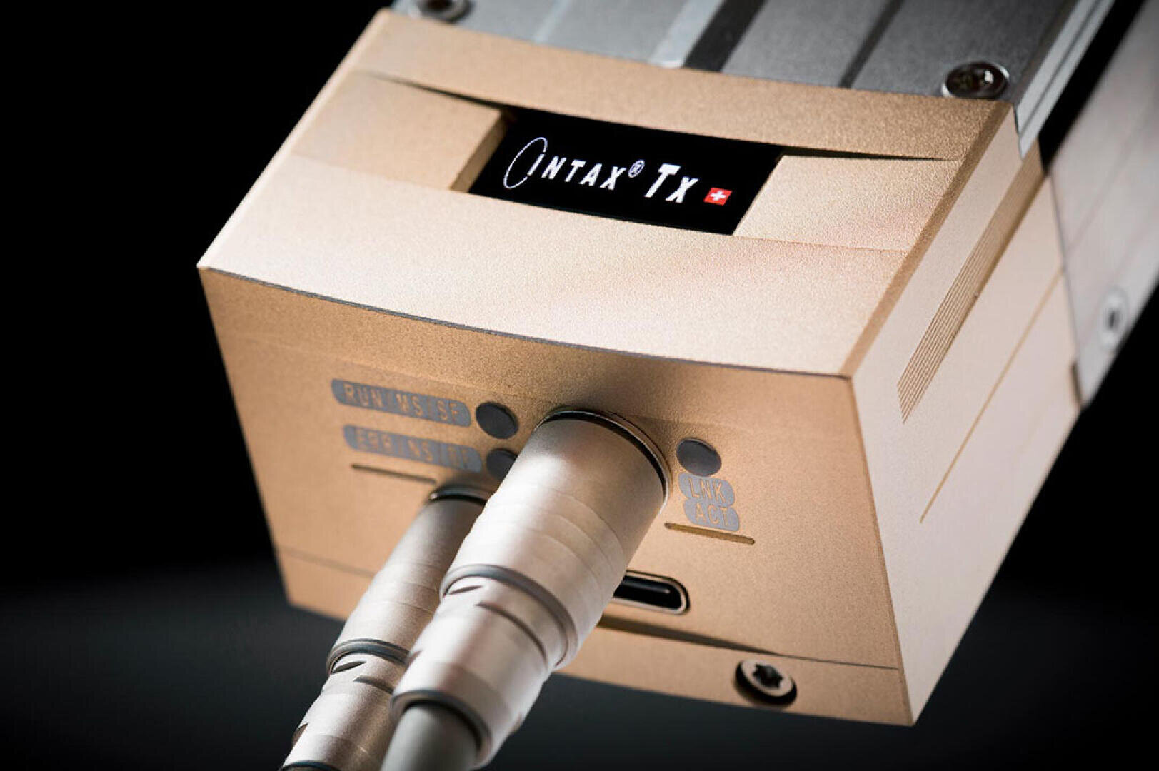 Nahaufnahme eines elektronischen Geräts aus Metall mit der Aufschrift "Qintax TX" auf dem Display, mit zwei Kabeln, die an die vorderen Anschlüsse angeschlossen sind, und einem USB-Anschluss darunter. Das Gerät hat ein schlankes, modernes Design mit einer matten Oberfläche.