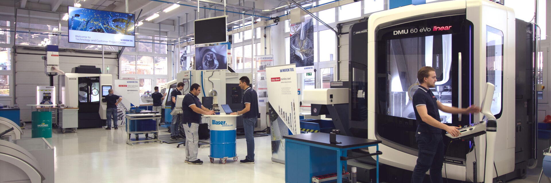 Eine moderne Industriewerkstatt mit mehreren Mitarbeitern, die in einer hellen, geräumigen Umgebung moderne Maschinen, digitale Bildschirme und Geräte bedienen.