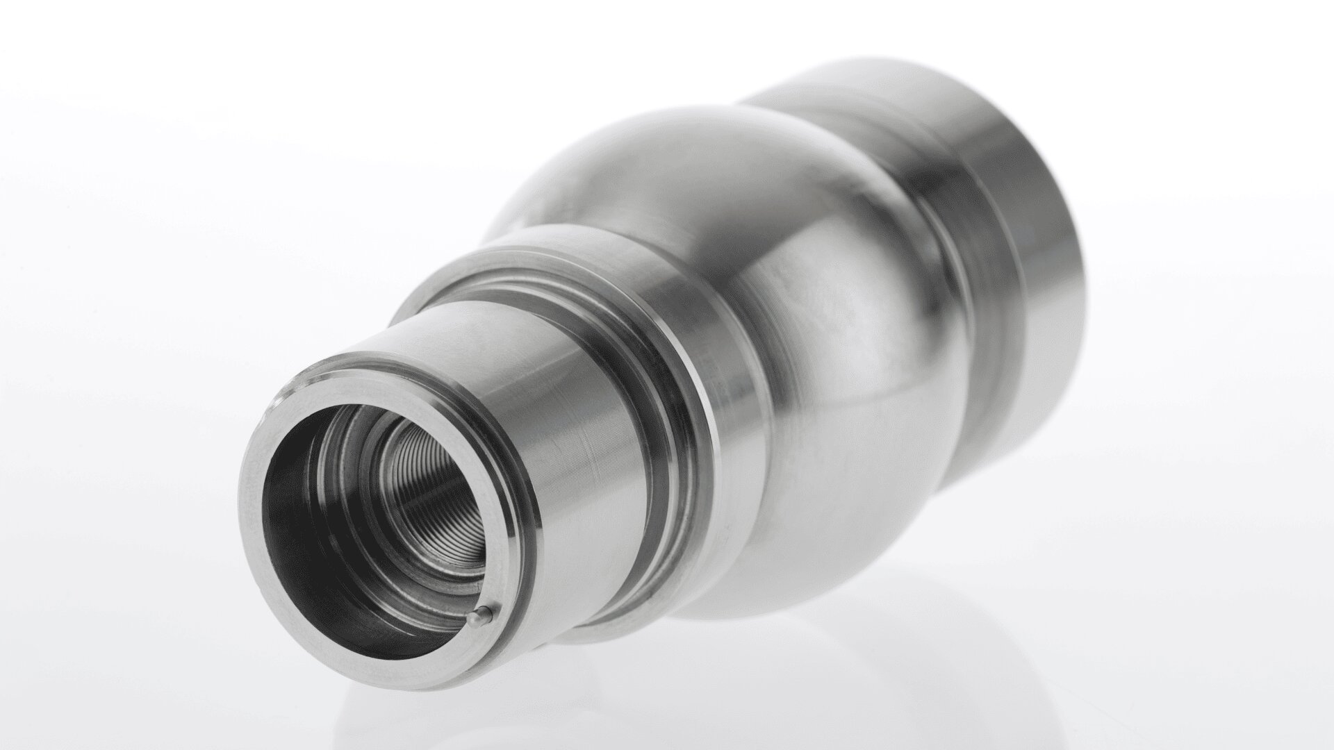 Ein glänzendes, maschinell bearbeitetes Metallteil mit zylindrischer Form, Innengewinde und abgerundeter zentraler Ausbuchtung vor einem schlichten weißen Hintergrund.