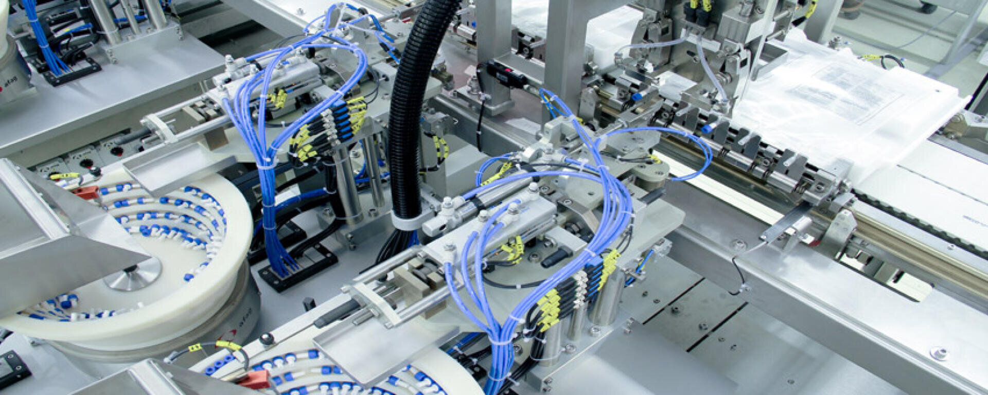 Close-up of an automated packaging machine with multiple robotic arms, blue cables, and conveyor belts handling products in a clean industrial environment.