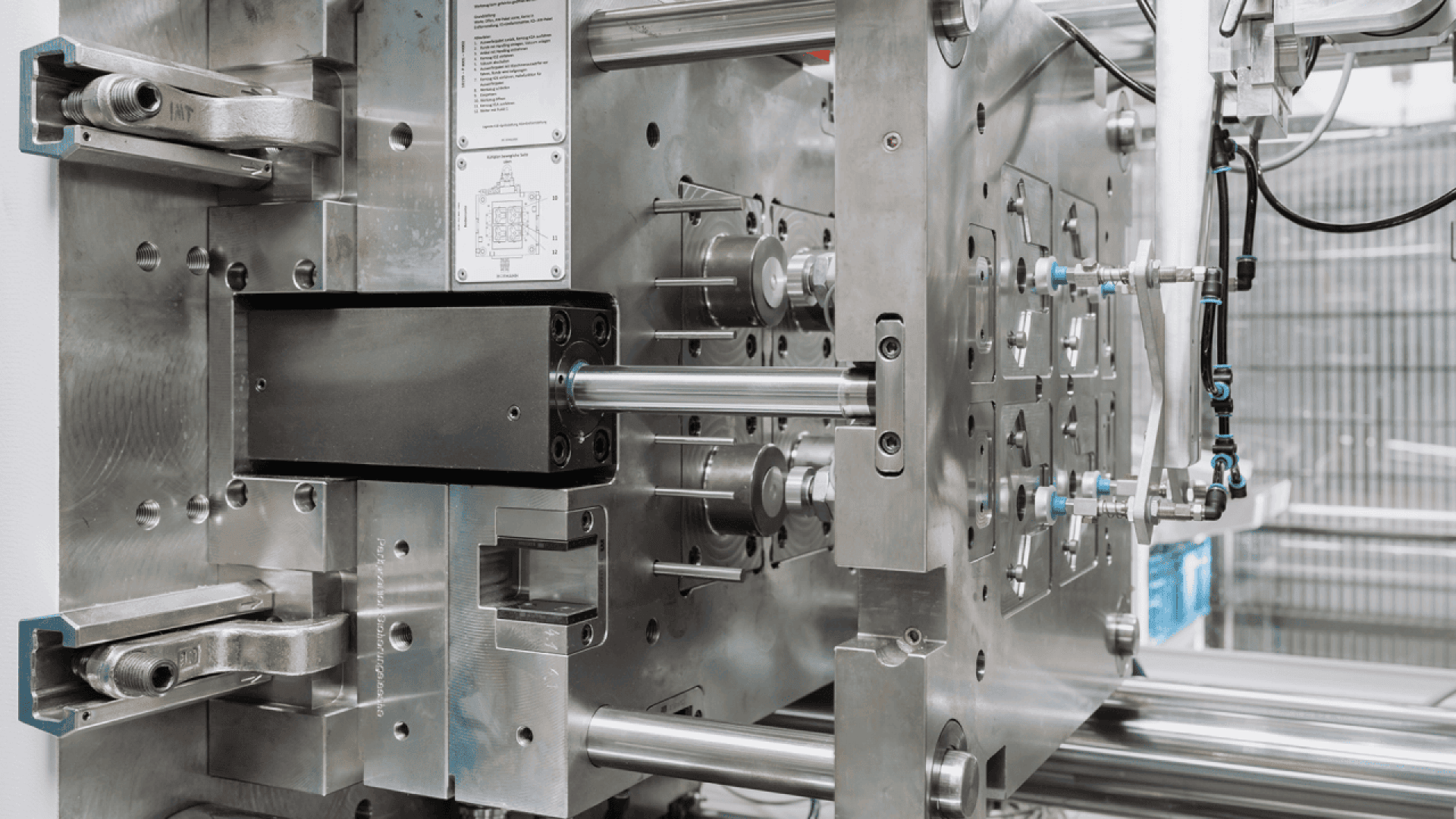 Close-up of an industrial injection molding machine showing metal plates, rods, and intricate mechanical parts used for shaping and forming plastic components.