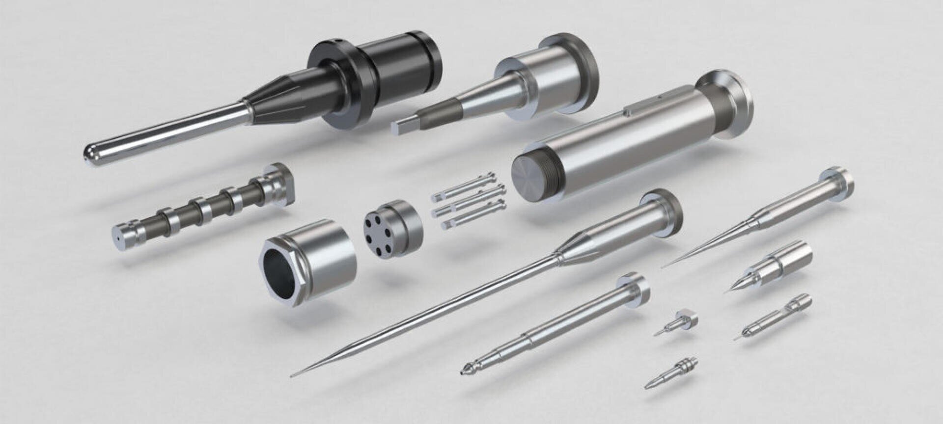 Auf einer hellgrauen Oberfläche sind verschiedene präzisionsgefertigte Metallteile, darunter Nadeln, Zylinder, Stangen und Verbindungsstücke, angeordnet. Die Teile haben eine polierte, metallische Oberfläche in Silber- und Schwarztönen.