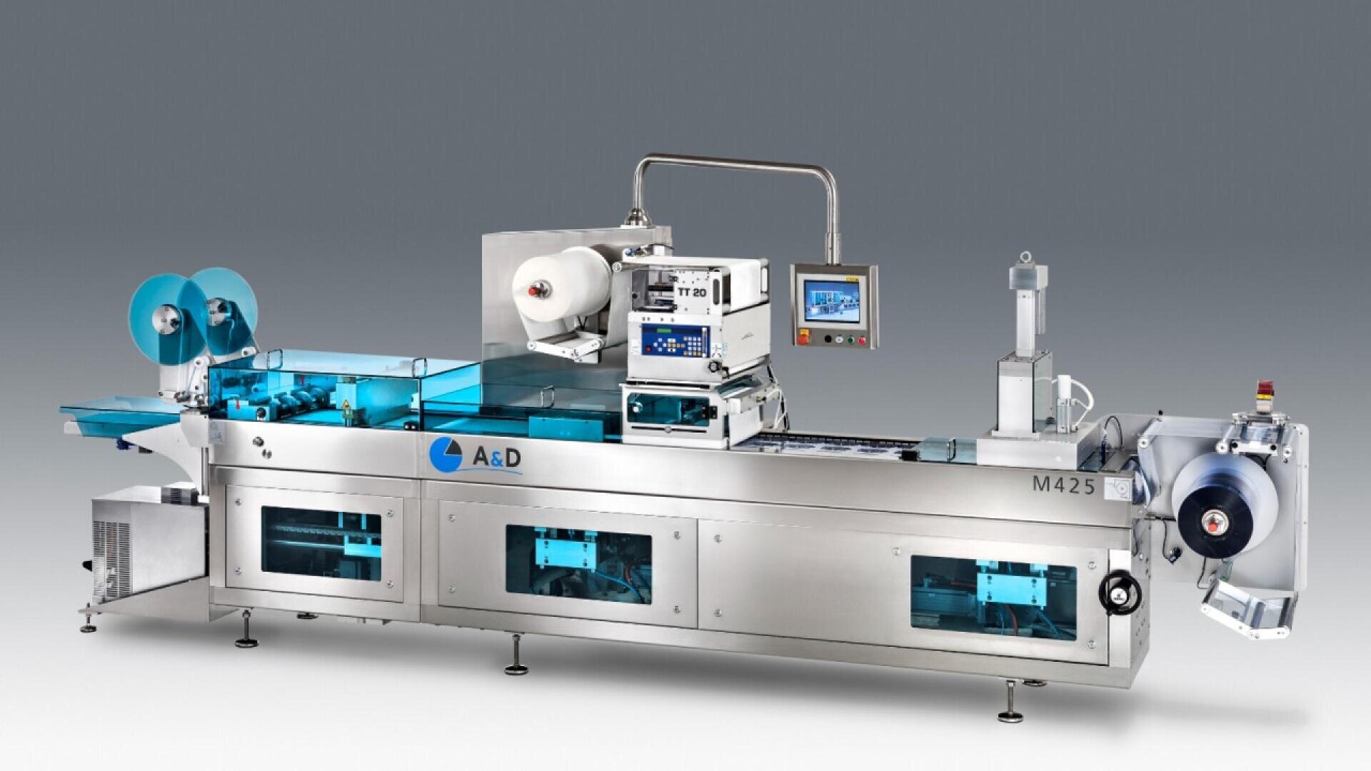 A modern industrial packaging machine with conveyor belts, rollers, control panels, and transparent blue covers, set against a plain gray background. The machine is labeled “M425” and “A&D.”.