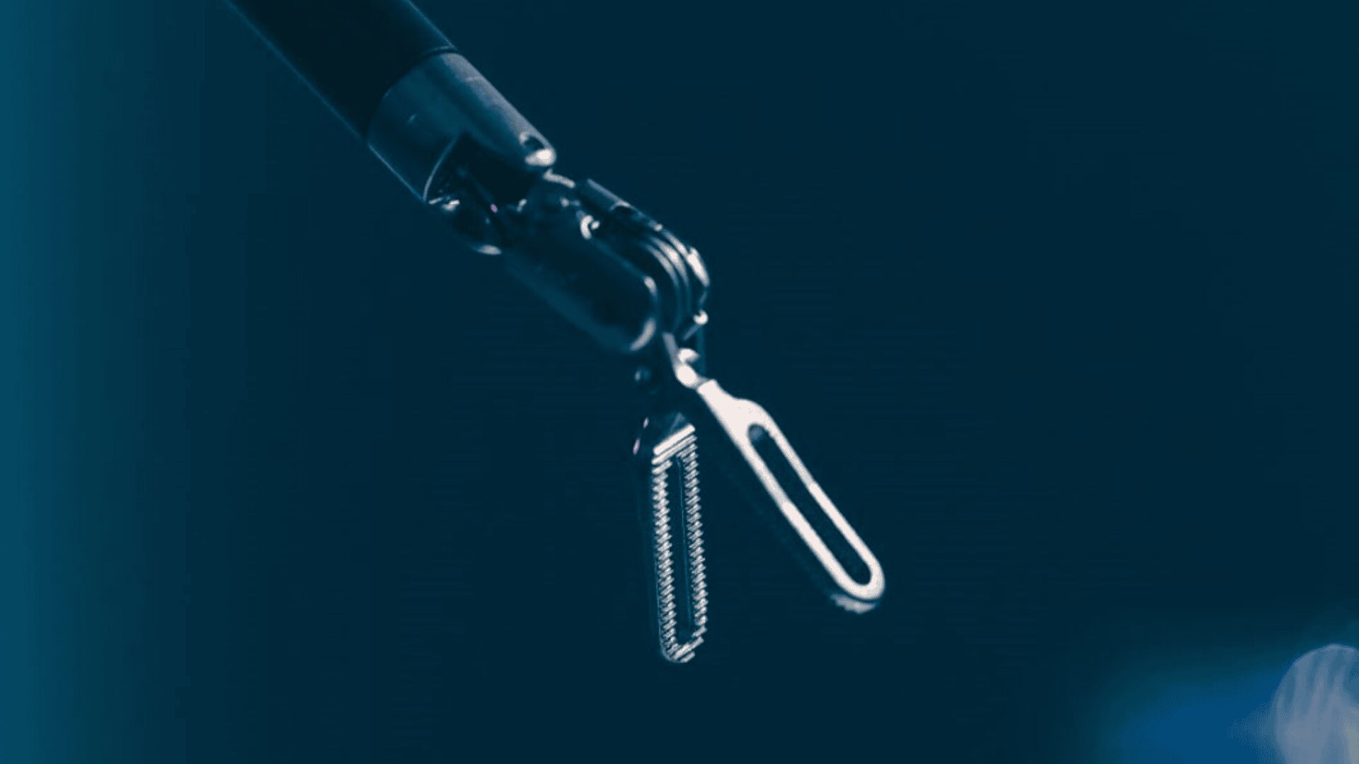 A robotic arm gripping a metallic tool, possibly surgical equipment, against a dark blue background. The focus is on the precise mechanism of the robotic hand and the tool it holds.
