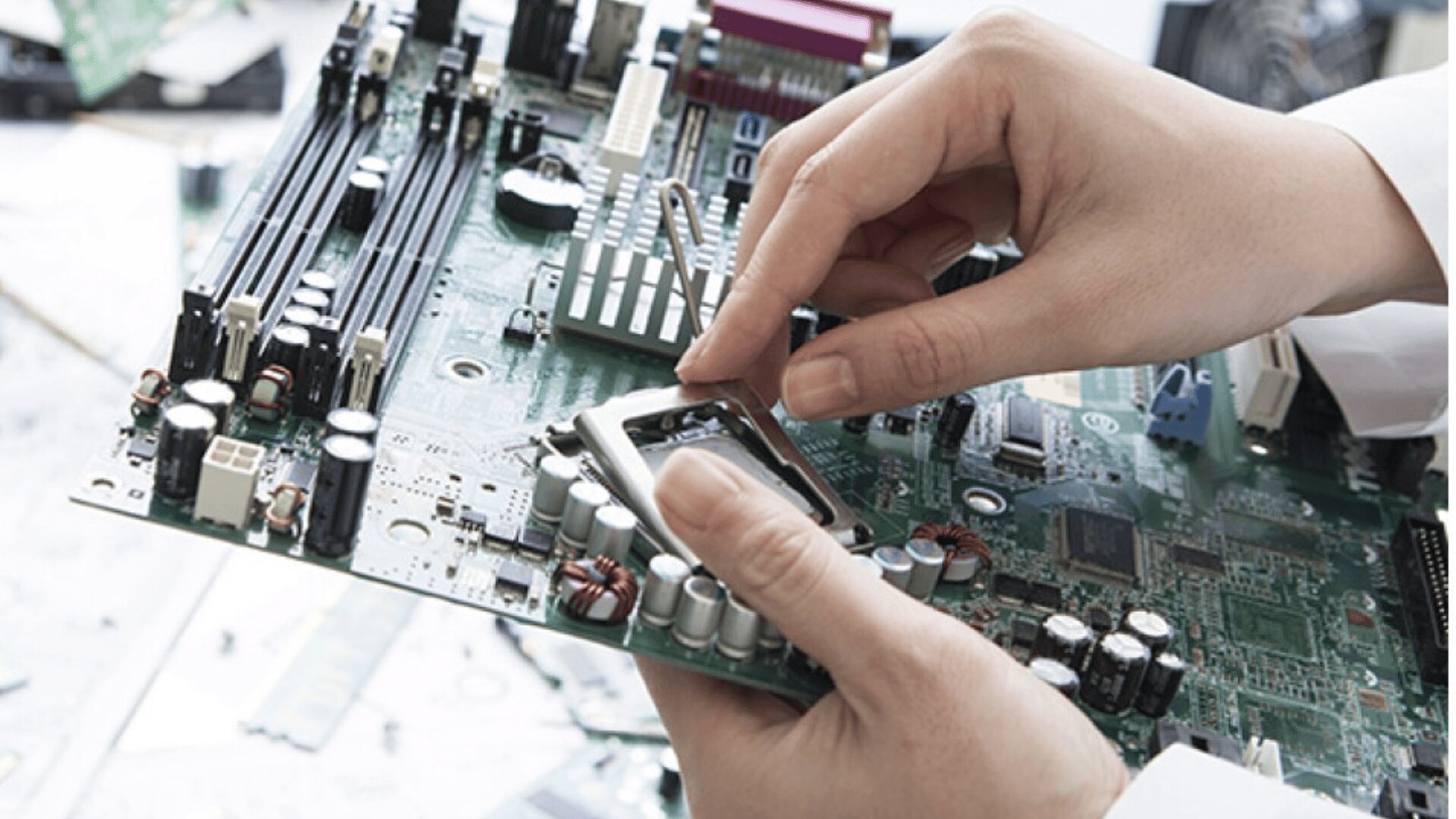 A person’s hands are installing or inspecting a computer processor socket on a green motherboard, surrounded by various electronic components and circuits.