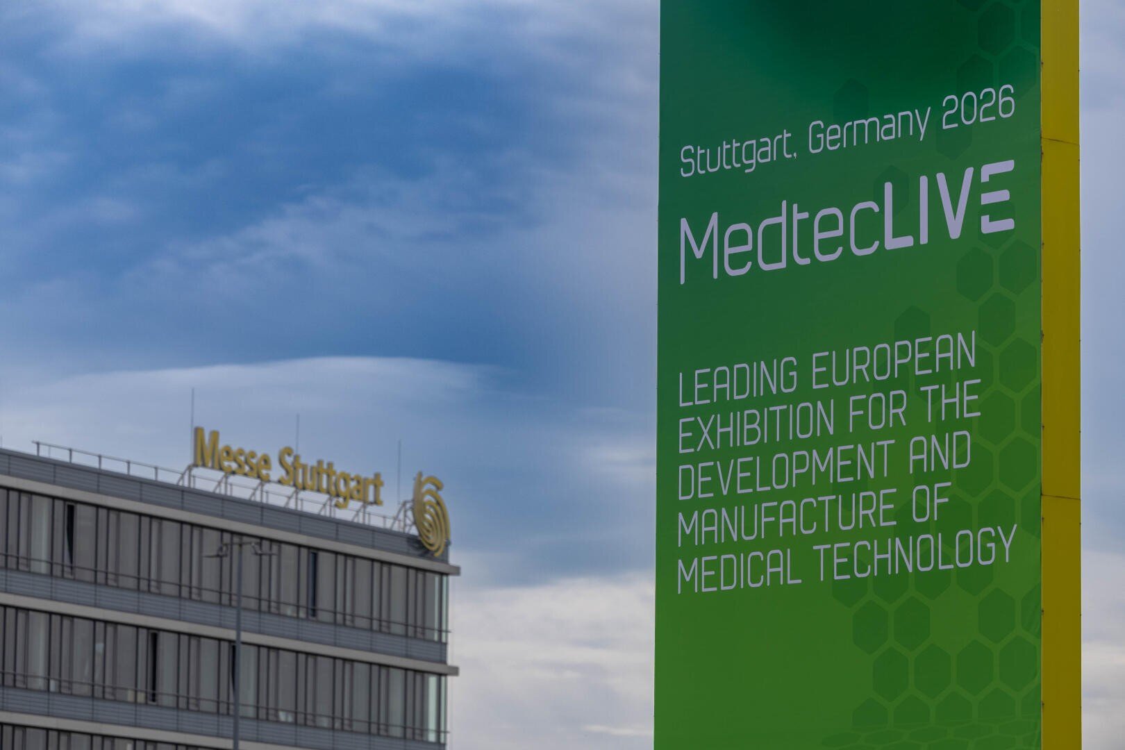 Großes grünes Schild, das für die MedtecLIVE 2026 in Stuttgart, Deutschland, wirbt, die als europäische Leitmesse für Medizintechnik beschrieben wird. Im Hintergrund ist das Gebäude der Messe Stuttgart unter einem bewölkten Himmel zu sehen.