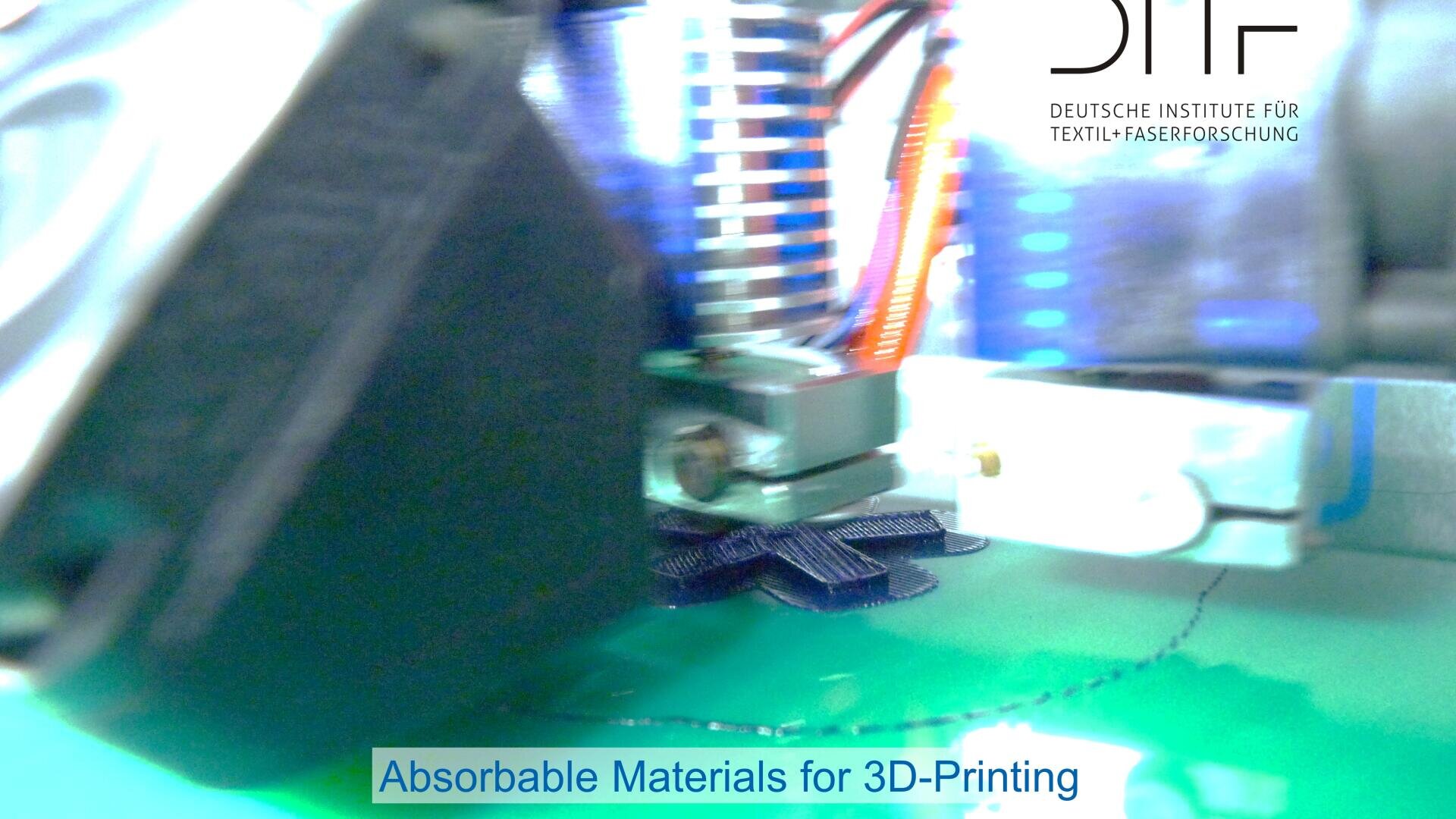 Close-up of a 3D printer creating an object with dark filament; background shows blurred machinery and wires. Text reads: Absorbable Materials for 3D-Printing and logo for German textile research institute (DITF).
