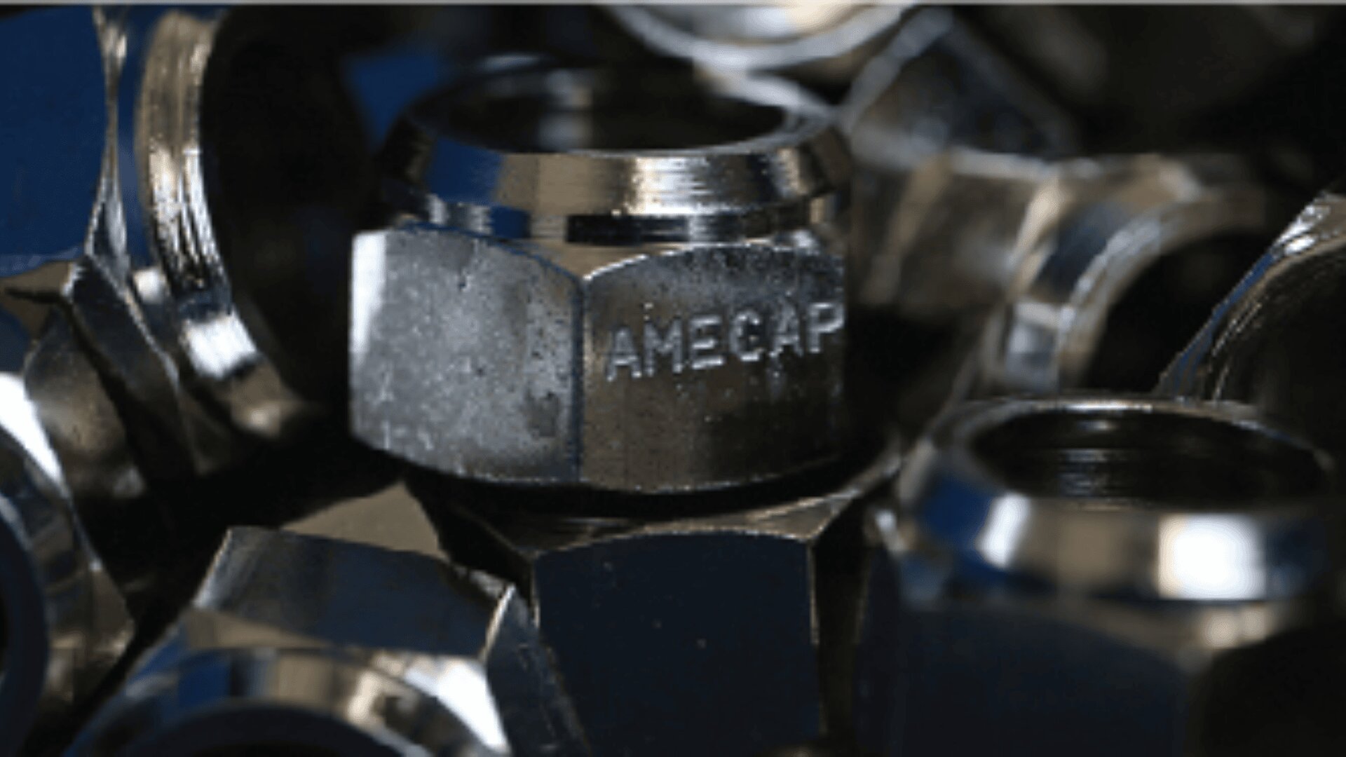 Eine Nahaufnahme mehrerer metallischer Sechskantmuttern. Auf einer davon ist deutlich das Wort „AMECAP“ eingraviert. Die Muttern haben eine glänzende, reflektierende Oberfläche.