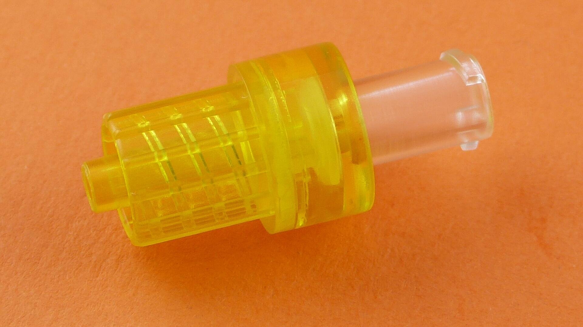 A small yellow translucent plastic piece with a cylindrical shape, grid-like texture on one end, and a clear connector on the other, placed on an orange background.