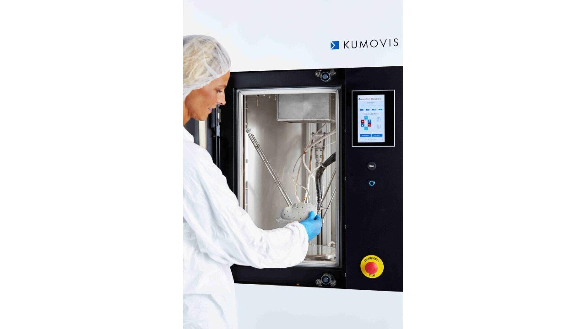 A person in protective clothing operates a Kumovis 3D printer, using blue gloves to handle a printed object inside the machine, with a digital control panel visible on the right.