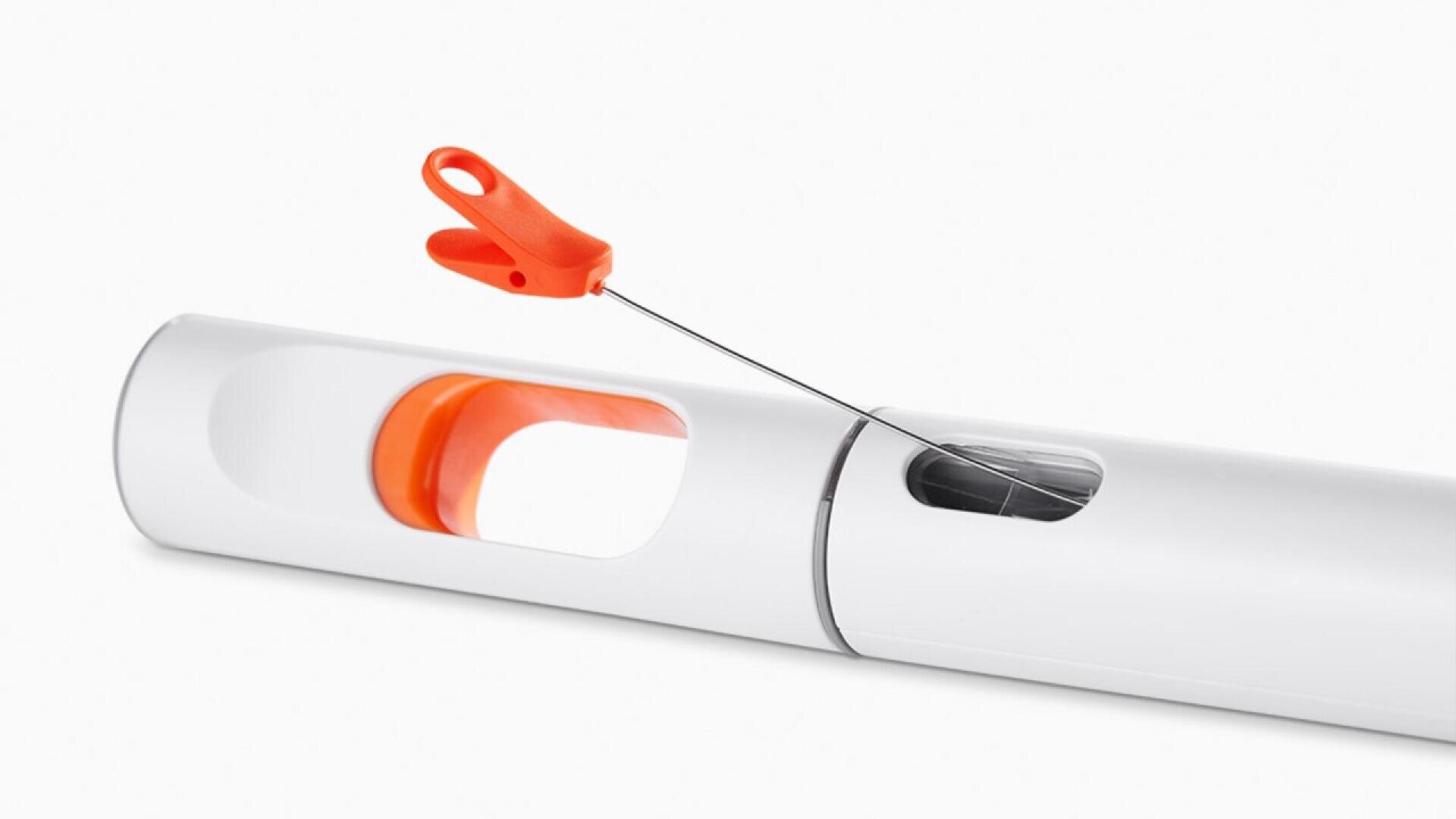 A white and orange tool with a long, thin metal wire ending in an orange plastic handle shaped like a clip, partially inserted into a white cylindrical casing with slots revealing the handle.