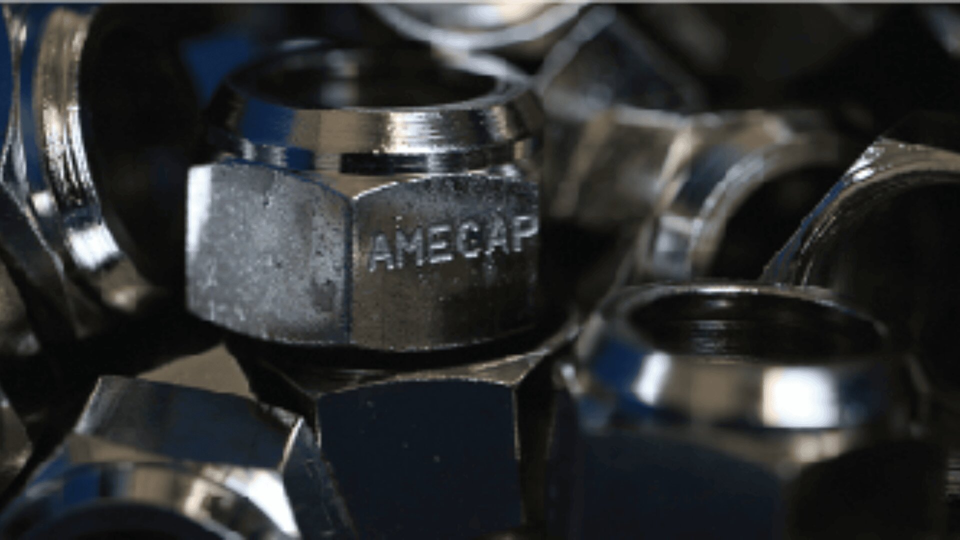 A close-up photo of several shiny metal nuts, with one prominently showing the engraved word “AMECAP” on its side. The image has a reflective and industrial appearance.