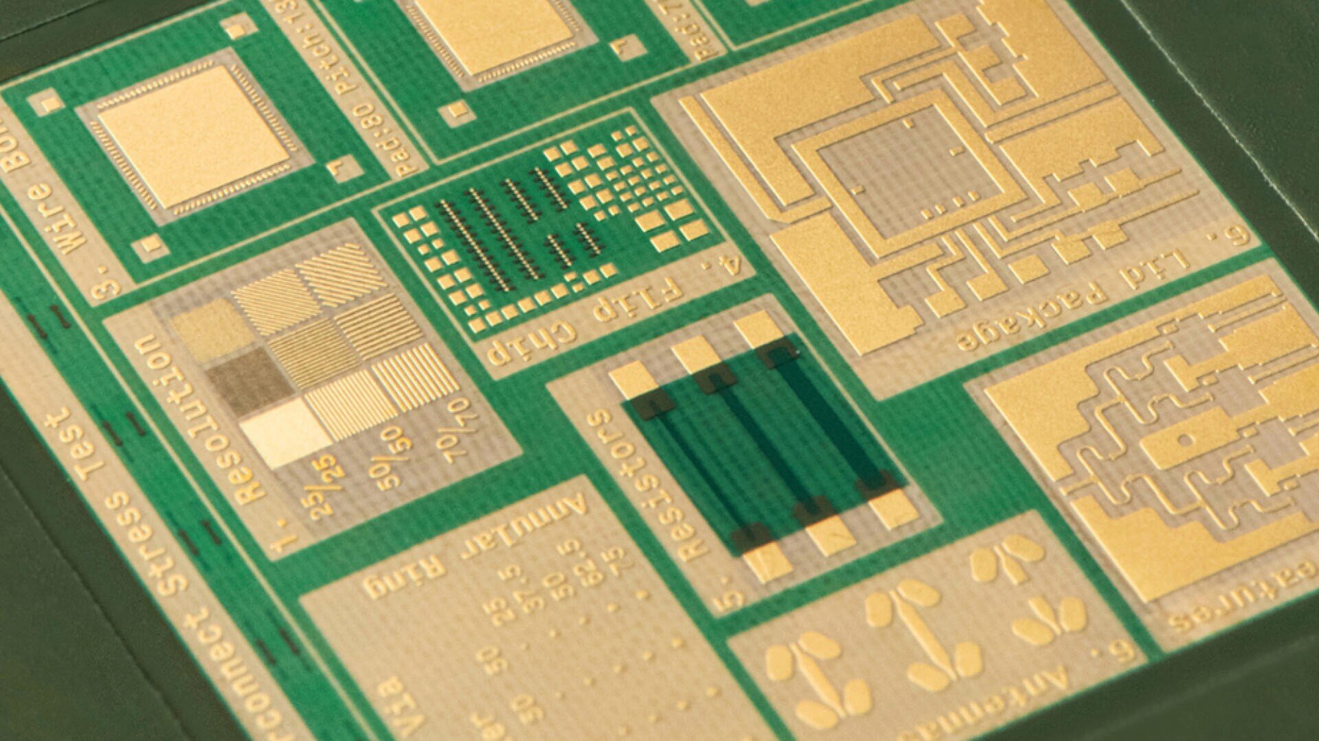 Close-up of a green and gold semiconductor test plate with various labeled sections, circuits and chip layouts used for testing and evaluating microchips.