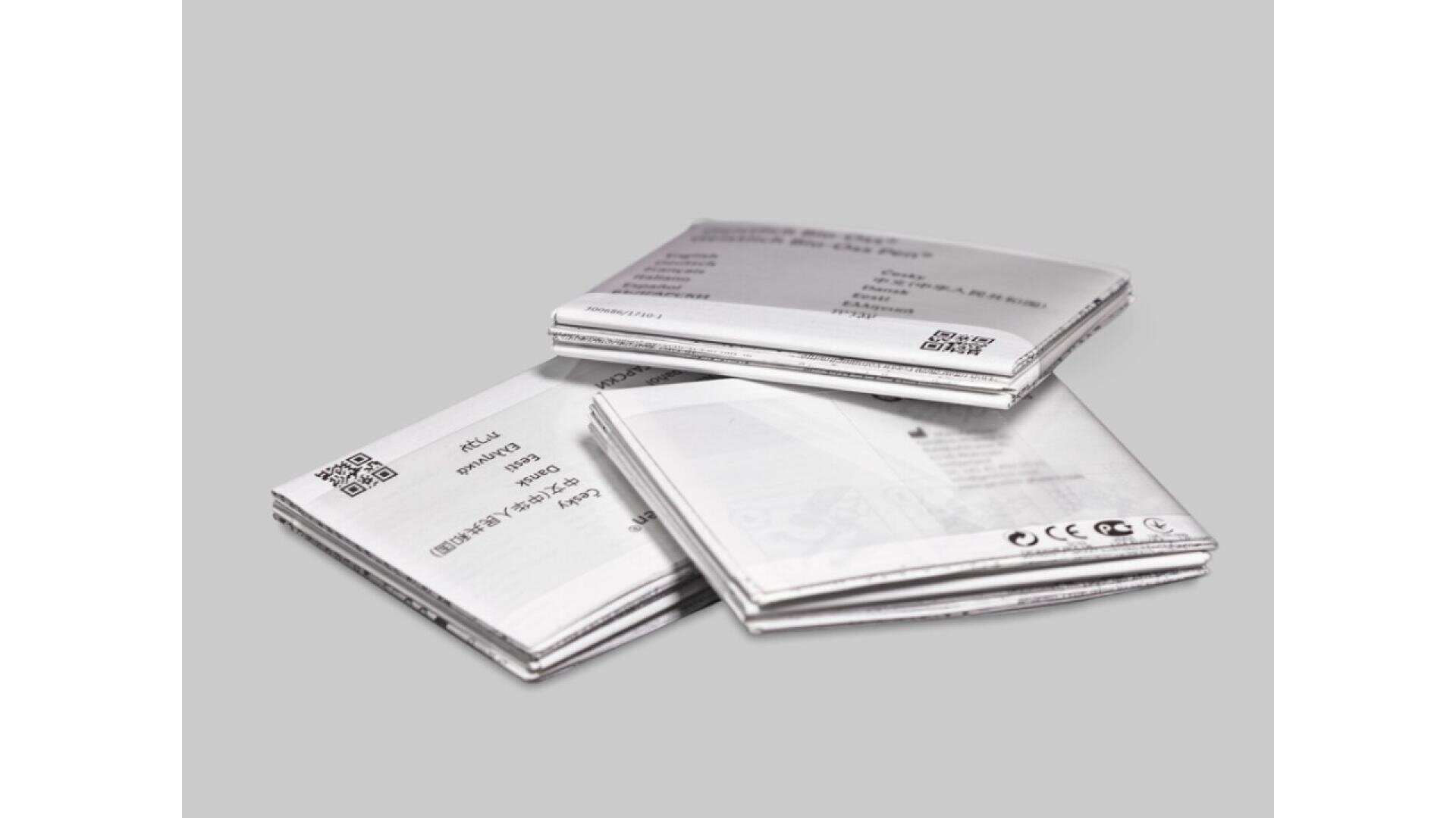 Four rectangular lithium batteries are stacked and scattered on a plain gray surface, each featuring printed text and QR codes on their metallic exteriors.