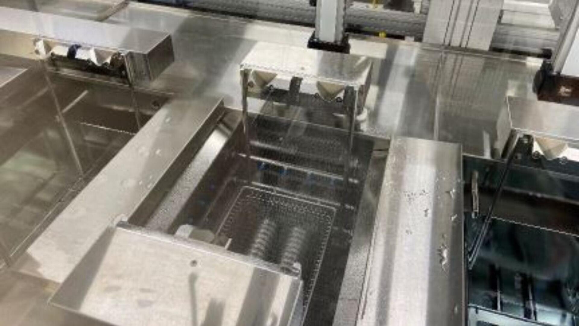 A close-up view of industrial stainless steel equipment, possibly used for food processing or manufacturing, featuring conveyor belts and machinery parts with clean, reflective surfaces.