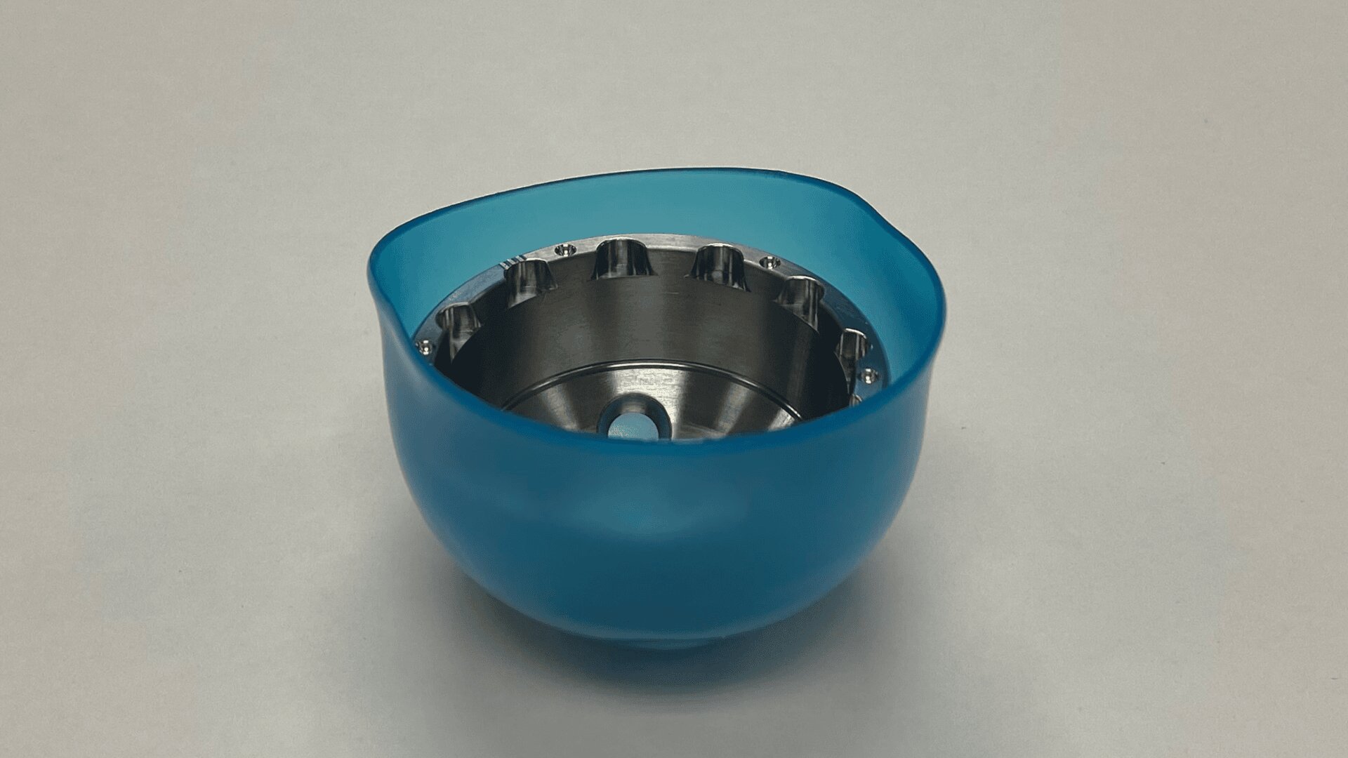 A blue plastic bowl with a metal insert featuring several small notches around the inner rim, placed on a plain light surface.