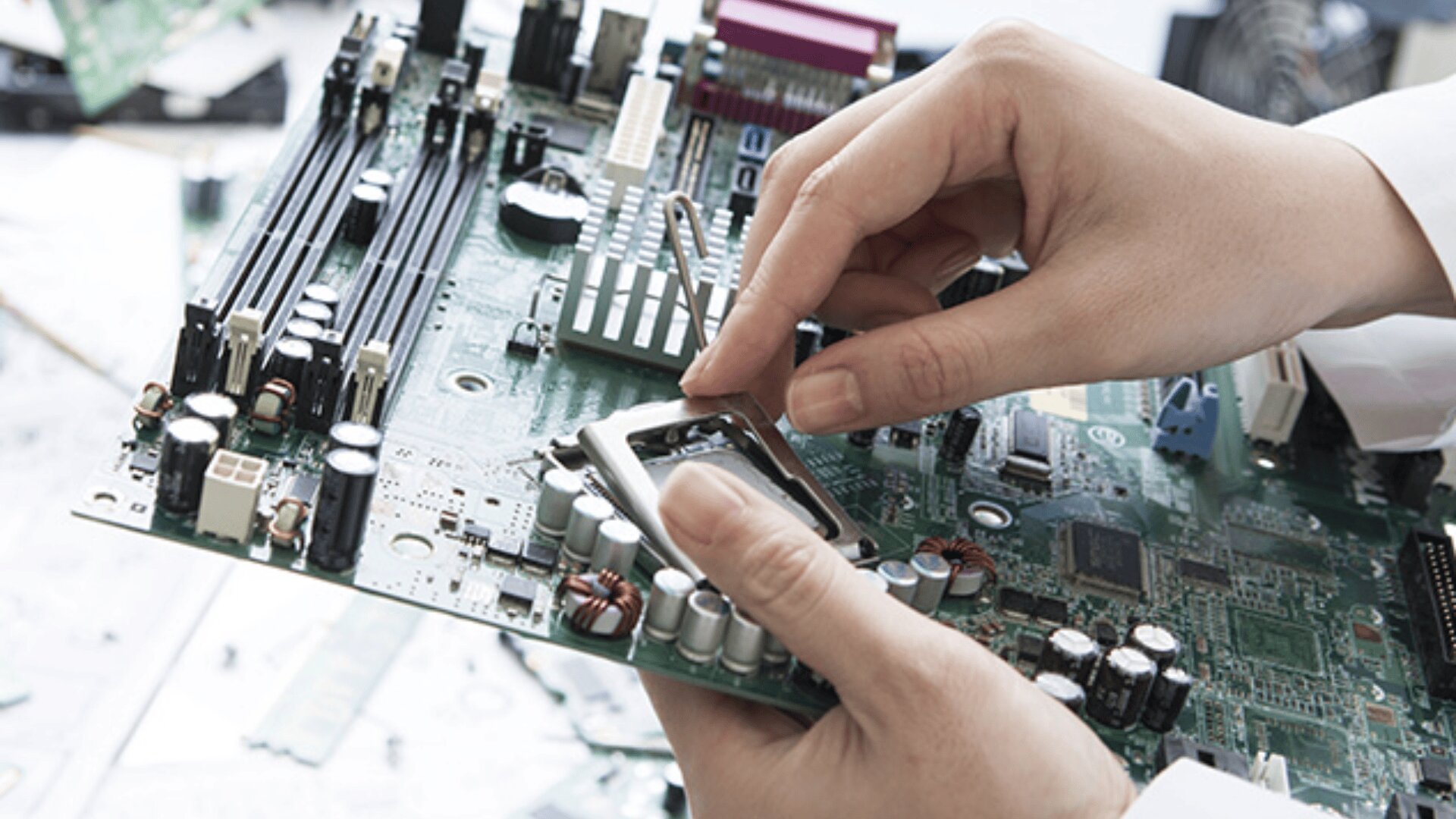 Die Hände einer Person installieren oder entfernen eine Komponente auf einer grünen Computerhauptplatine, die von verschiedenen elektronischen Teilen und Schaltkreisen umgeben ist.