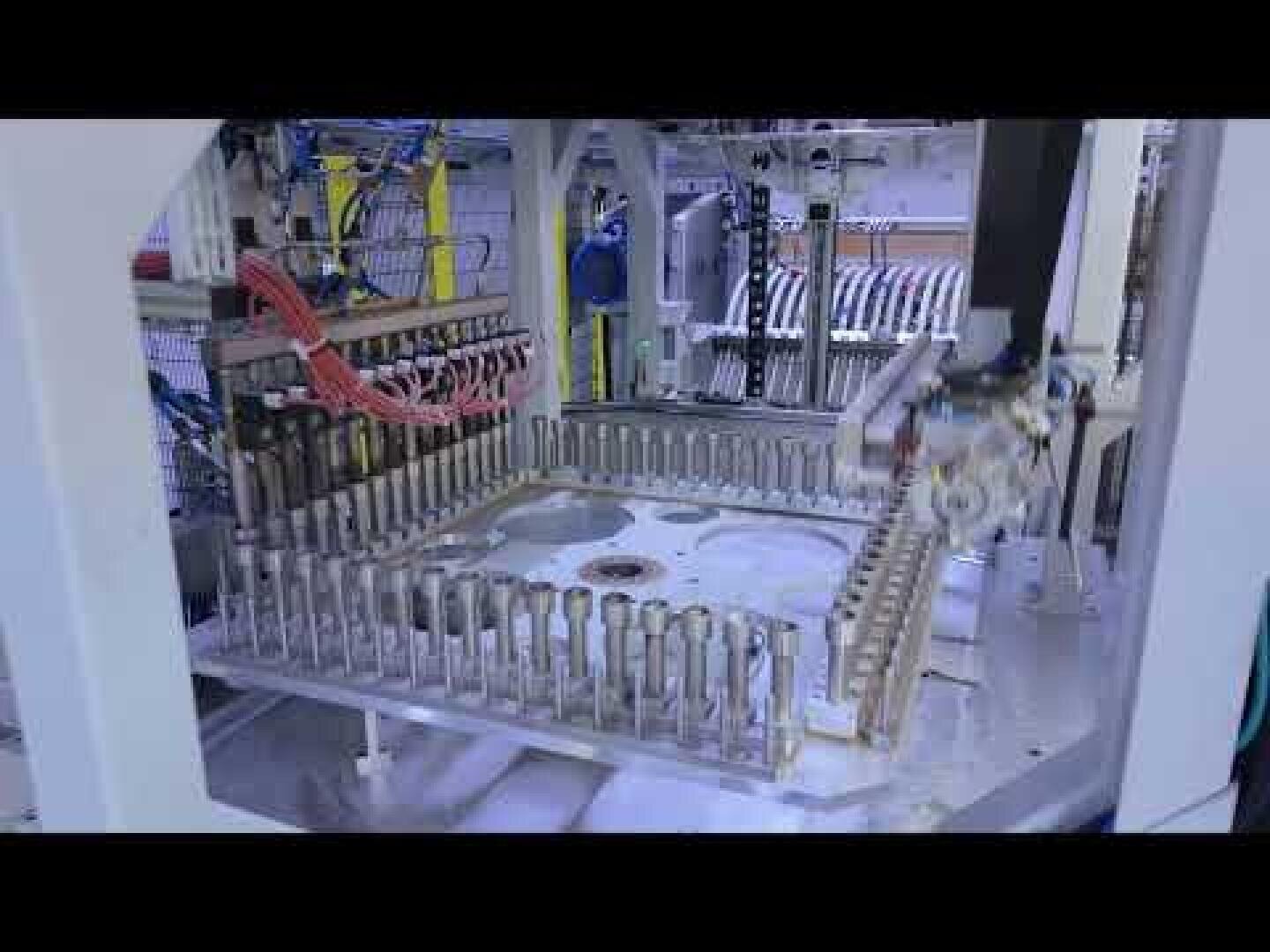 Eine Nahaufnahme von automatisierten Industriemaschinen mit Roboterarmen, die in einer Fabrikhalle Metallteile zusammenbauen oder handhaben, umgeben von mechanischen Komponenten und Kabeln.