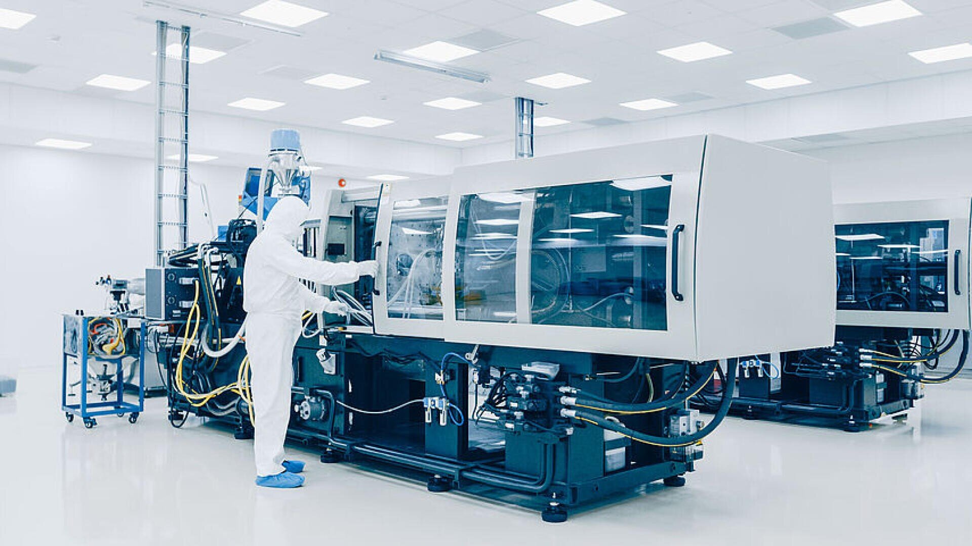Eine Person in einem kompletten Reinraumanzug bedient eine große, moderne Industriemaschine in einer hellen, sterilen Produktionsstätte.