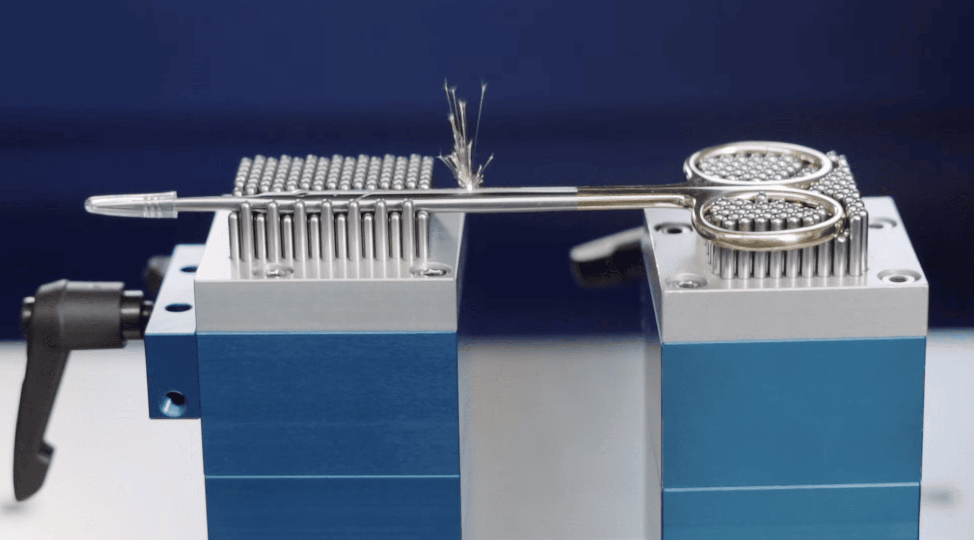 Scissors balancing on two blue metal platforms with magnetic arrays, while a feather rests on the scissors with its fibers spreading outward.