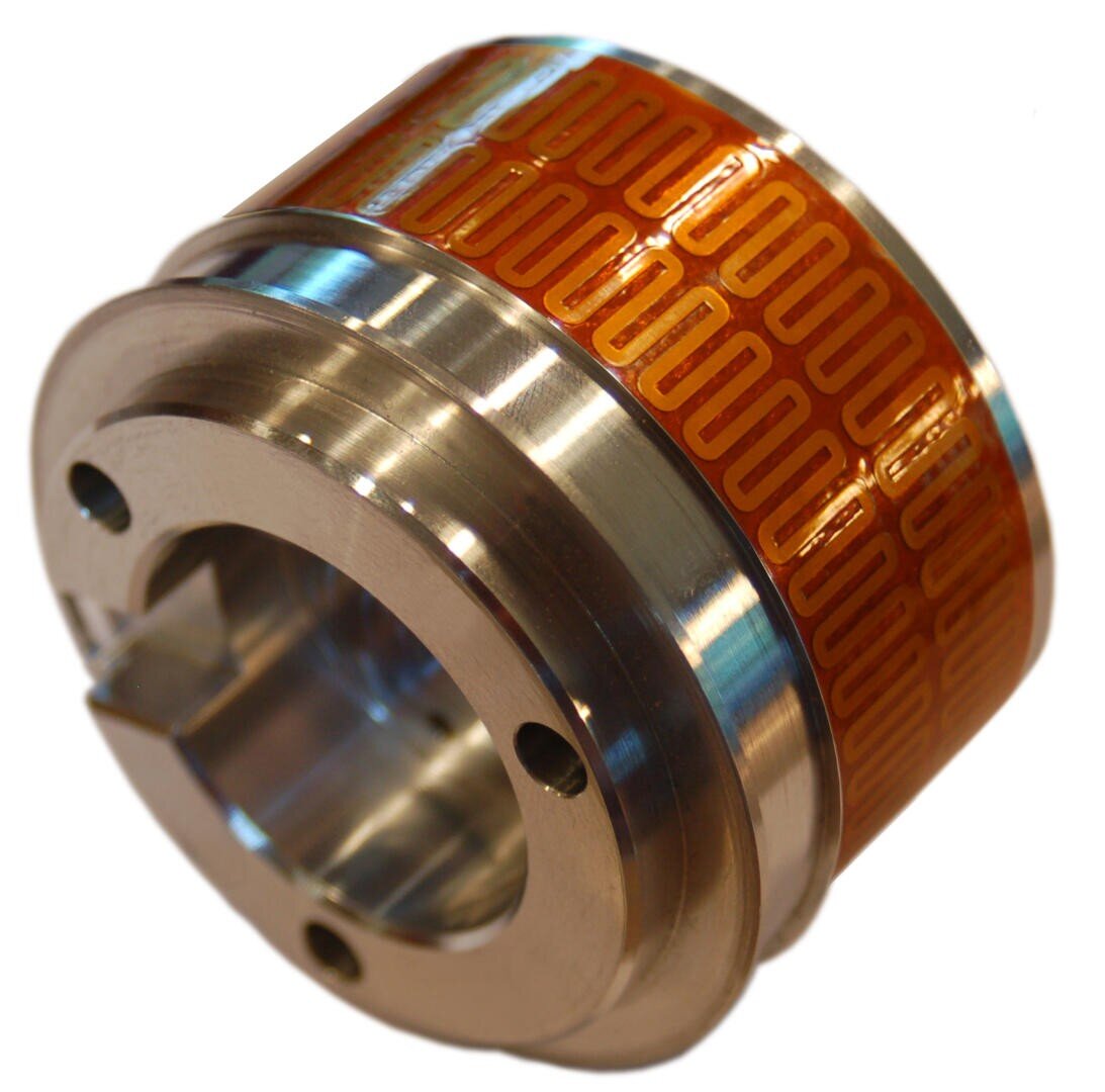 A cylindrical metal component with a shiny finish, featuring an orange flexible circuit or heating element wrapped around the outer surface. The element has a repeating rectangular pattern.