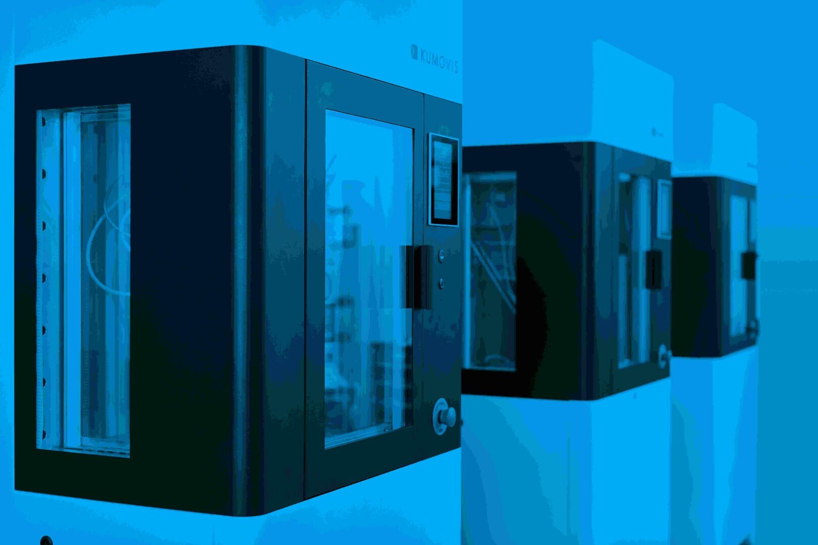 Nahaufnahme von zwei modernen, schwarz-weißen Industriemaschinen mit Glastüren, nebeneinander in einer hell erleuchteten, blau getönten Umgebung.