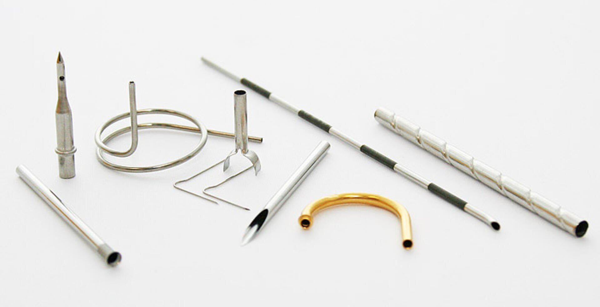 A variety of small metal parts, including coils, rods, tubes, and a curved gold tube, are arranged on a white background.