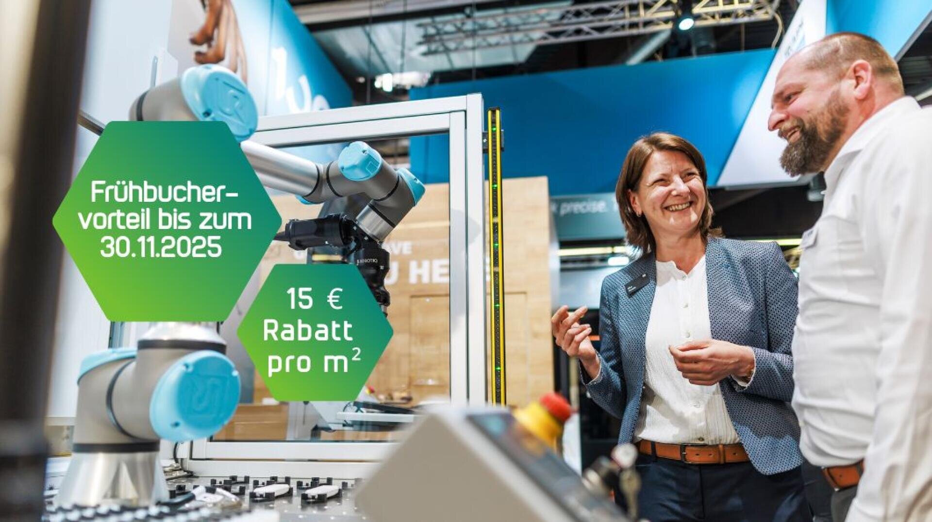 Eine Frau und ein Mann lächeln und unterhalten sich neben einem Roboterarm auf einer Technologieausstellung. Grüne Sechseck-Banner zeigen an: Frühbuchervorteil bis zum 30.11.2025 und 15 € Rabatt pro m².