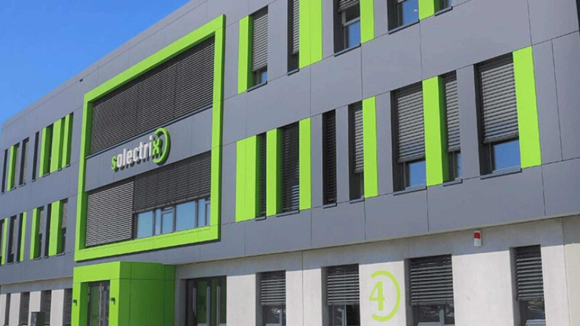 Modernes graues Gebäude mit hellgrünen Akzenten und dem Solectrix-Logo an der Fassade; große Fenster mit Fensterläden und eine „4“ in einem grünen Kreis in der Nähe des Eingangs.