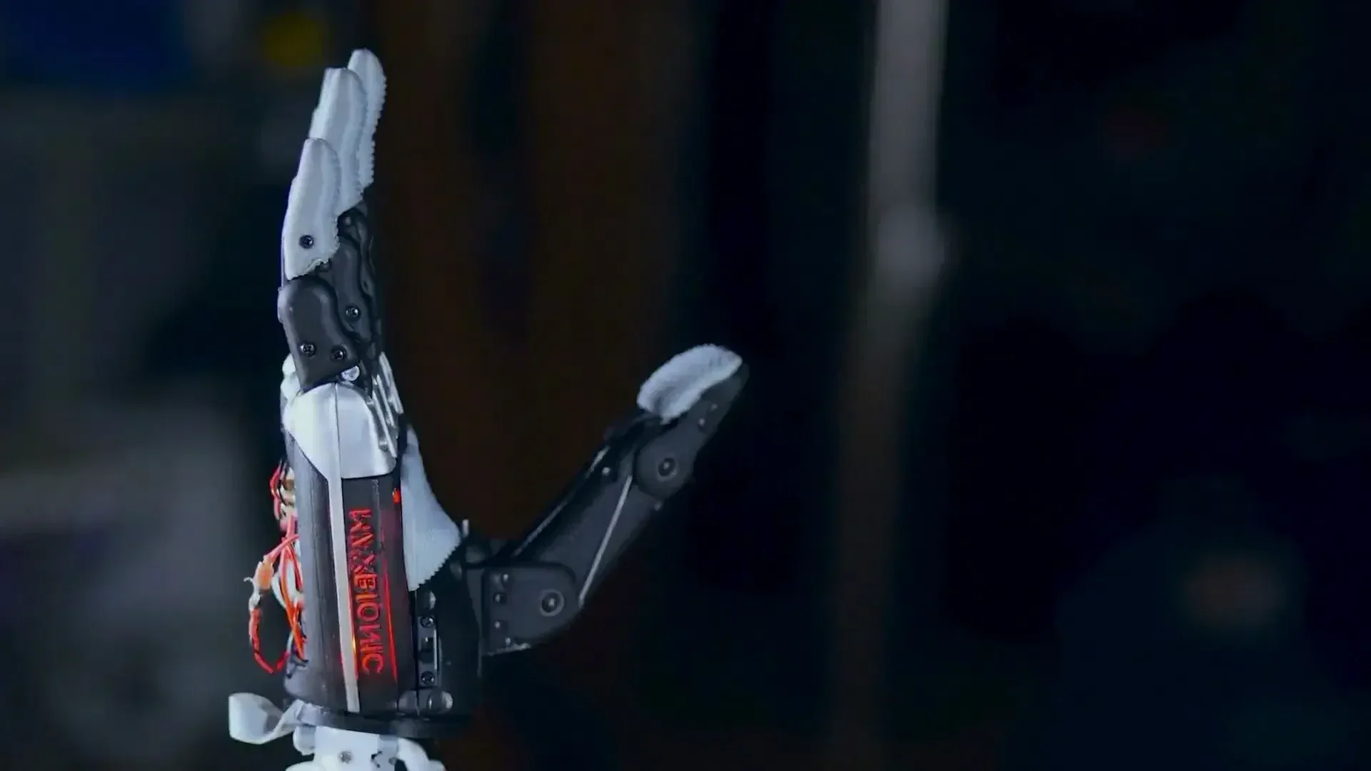 Eine schwarz-weiße Roboterhand mit sichtbarer Verkabelung und mechanischen Gelenken ist aufrecht aufgestellt, die Handfläche zeigt nach links und die Finger sind ausgestreckt. Das Wort KYBOTIC ist an der Seite in roten Buchstaben zu sehen. Der Hintergrund ist dunkel und unscharf.