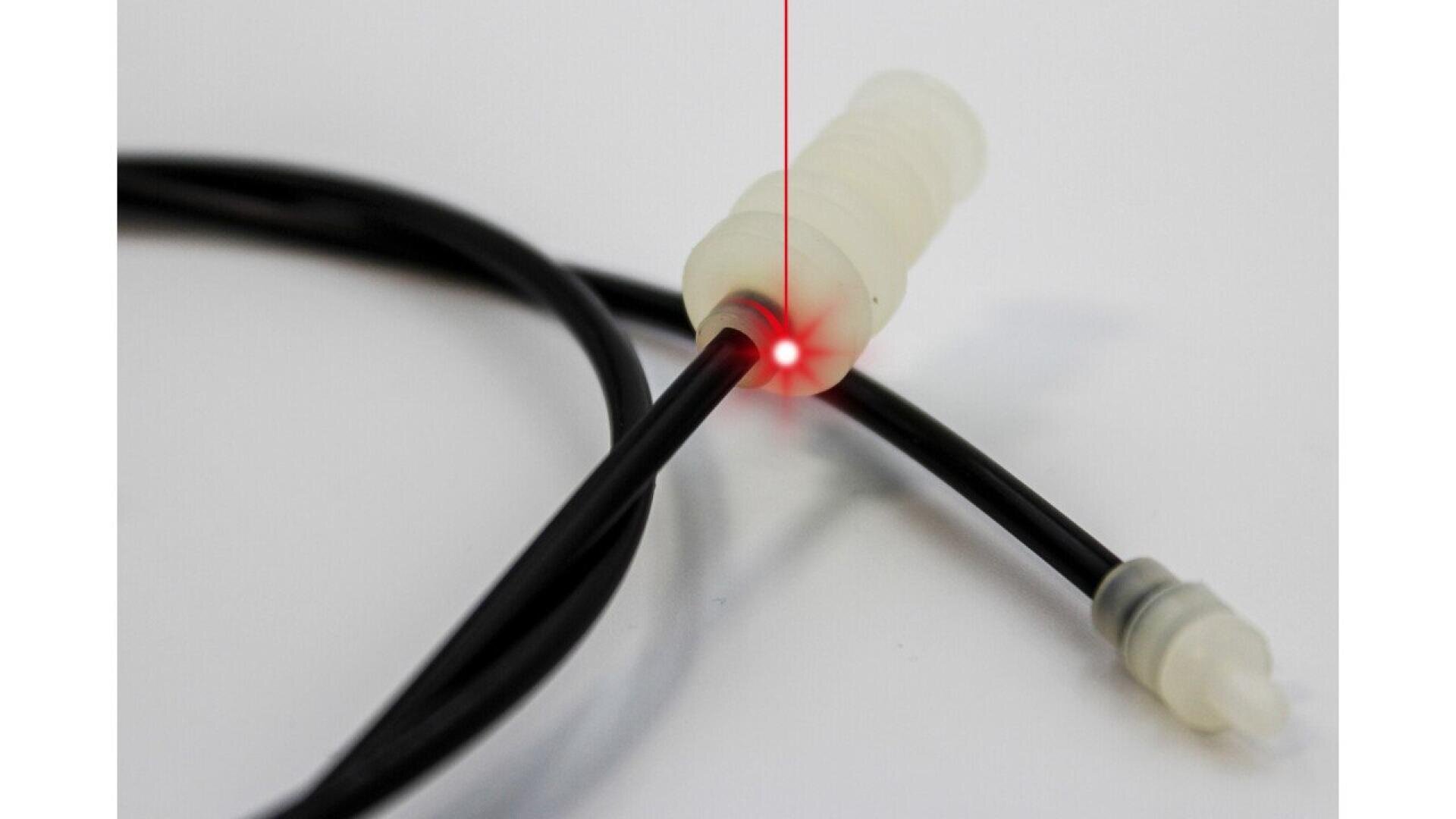Close-up of a black cable connected to a white plastic connector, with a red laser beam and bright red point of light at the connection, on a white background.