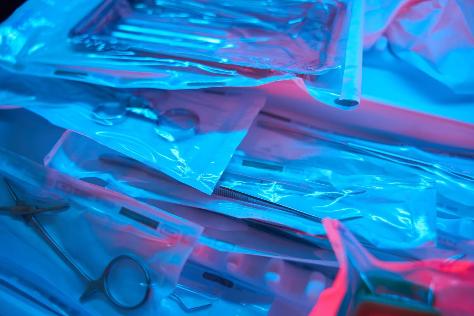 Sterilized dental or medical instruments, sealed in a transparent plastic package, illuminated with blue and pink light, are placed in a clinical environment and prepared for use in a procedure.