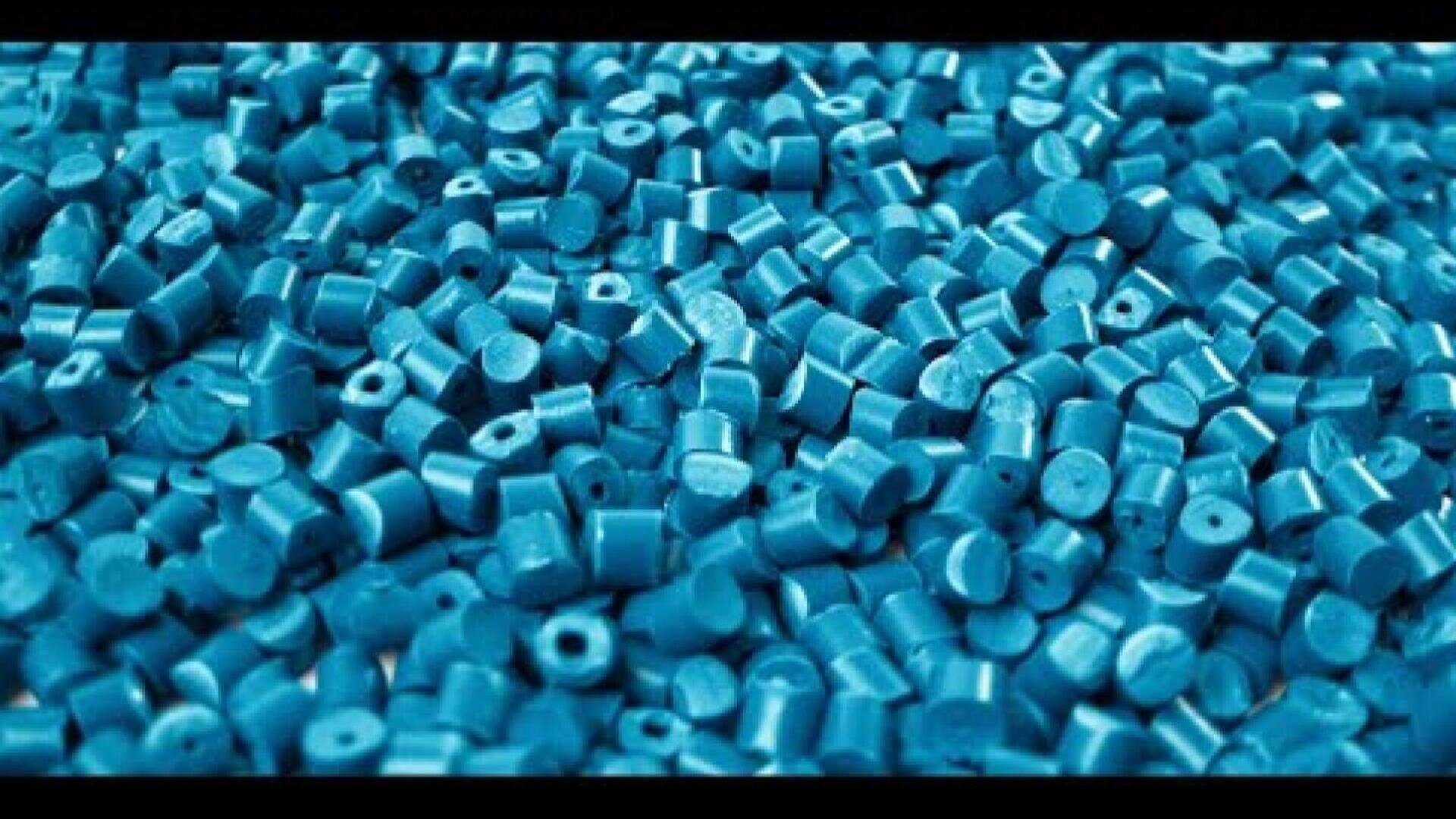 A close-up view of a large pile of small, round, blue plastic pellets, typically used as raw material in plastic manufacturing.