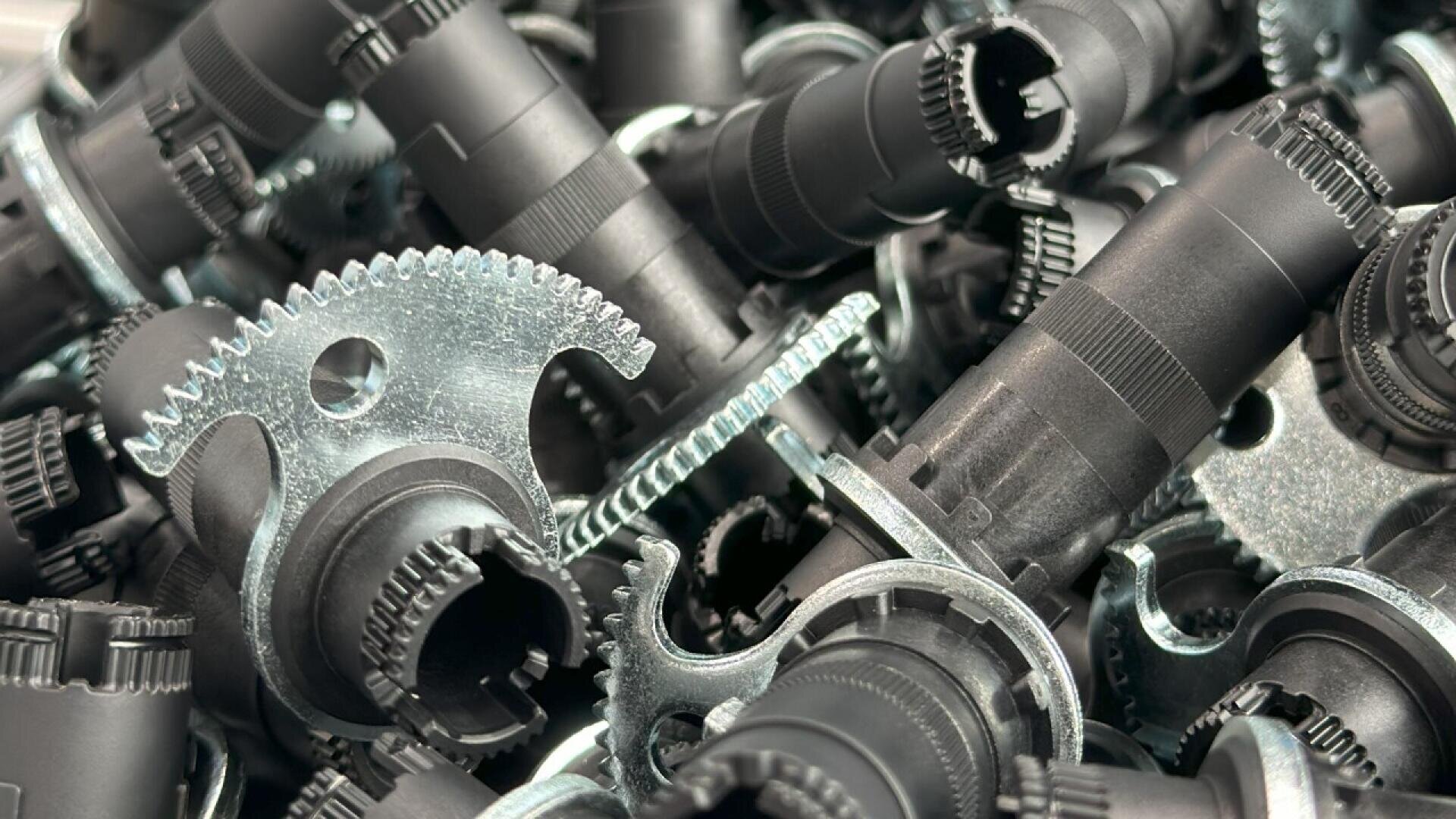 A close-up view of a pile of metal and plastic mechanical gears and cylindrical components, showcasing intricate teeth and industrial design details.