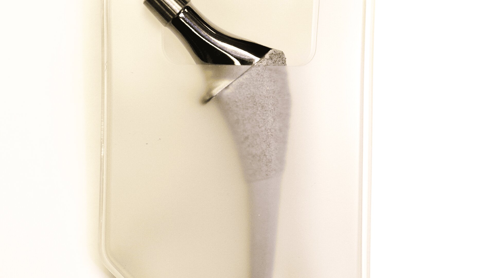 A metallic orthopedic hip implant is encased in a clear packaging, displayed against a plain white background.