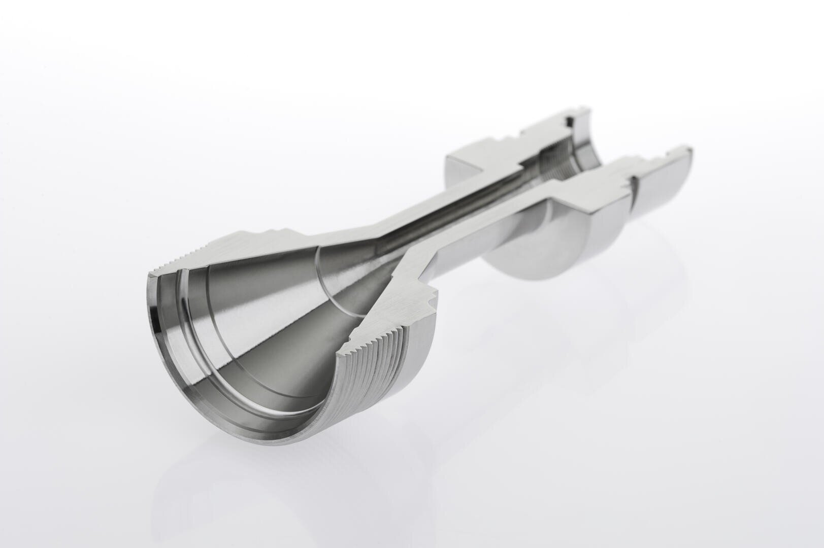 A metal mechanical part with a symmetrical, cylindrical shape, featuring a cutaway section to reveal internal grooves, threads, and chambers, displayed on a white background.