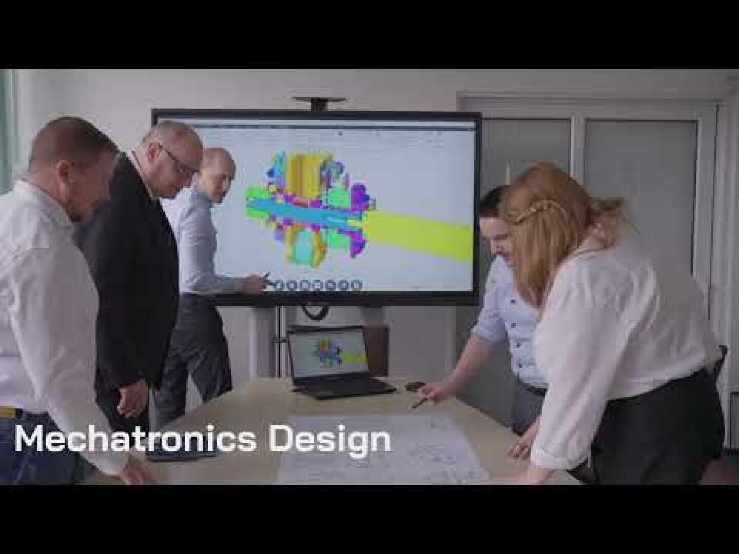 Five people gather around a table reviewing blueprints, with a large screen behind them displaying a colorful 3D mechanical model. Text on the image reads Mechatronics Design.