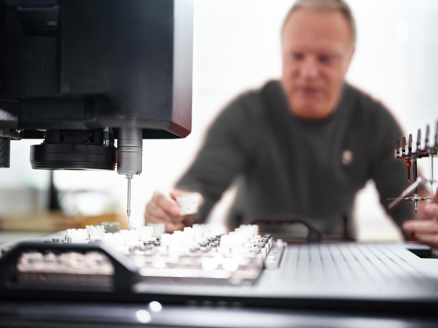 A person operates precision equipment in a laboratory setting, focusing on a machine with small components on a grid, while the background is blurred to highlight the detailed work.