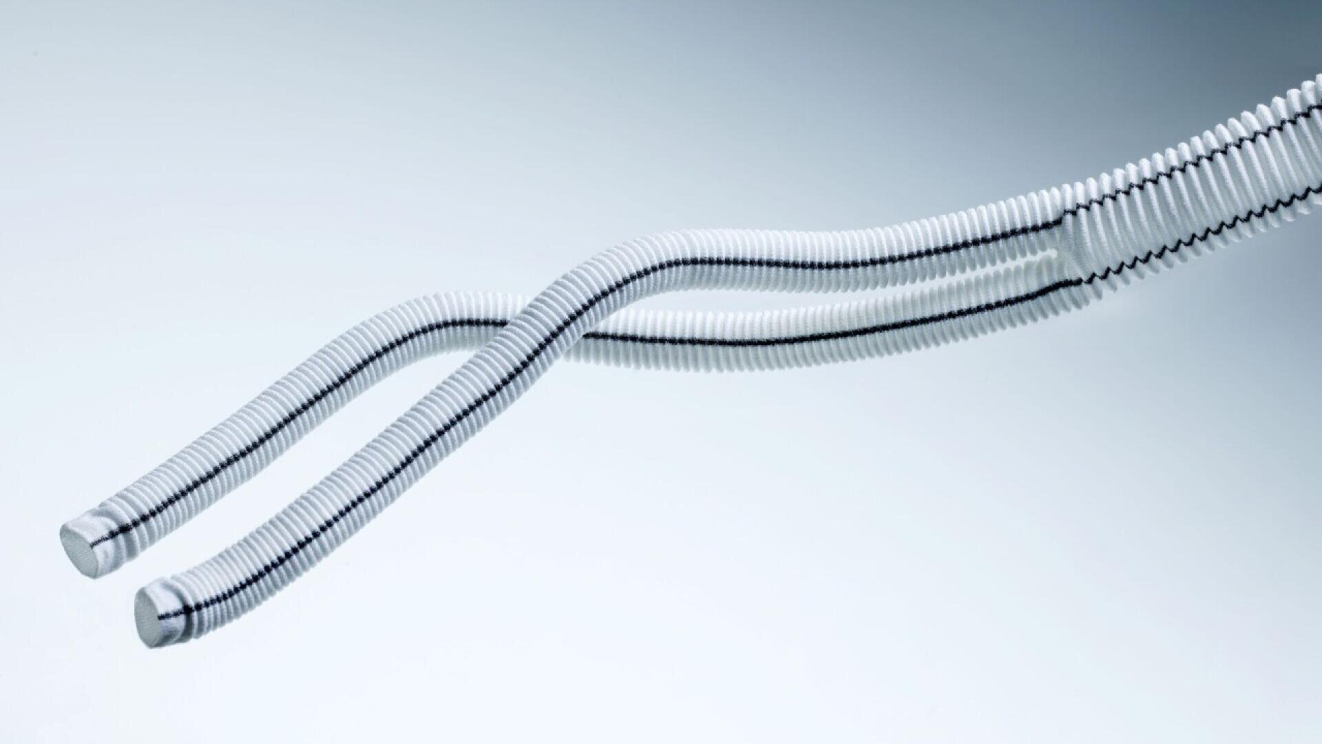Two flexible, ribbed white medical tubes with black stripes run parallel, with one branch splitting into two. They are photographed on a smooth, gradient gray background.