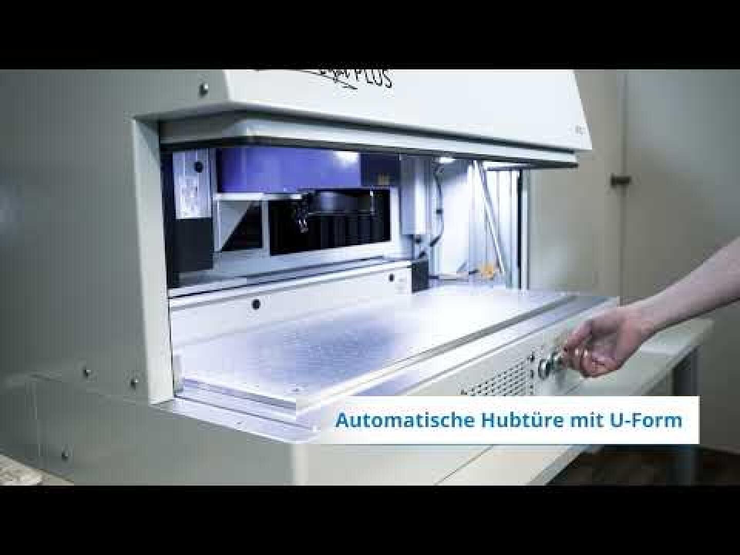 Die Hand einer Person bedient eine Maschine mit einem Schiebetablett und beleuchtetem Innenraum. Ein deutsches Etikett auf dem Bildschirm lautet Automatische Hubtüre mit U-Form.