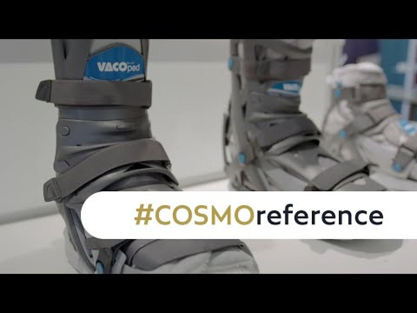 Nahaufnahme von grauen orthopädischen Wanderschuhen mit der Aufschrift VACOped. In großen Buchstaben steht #COSMOreference darüber.