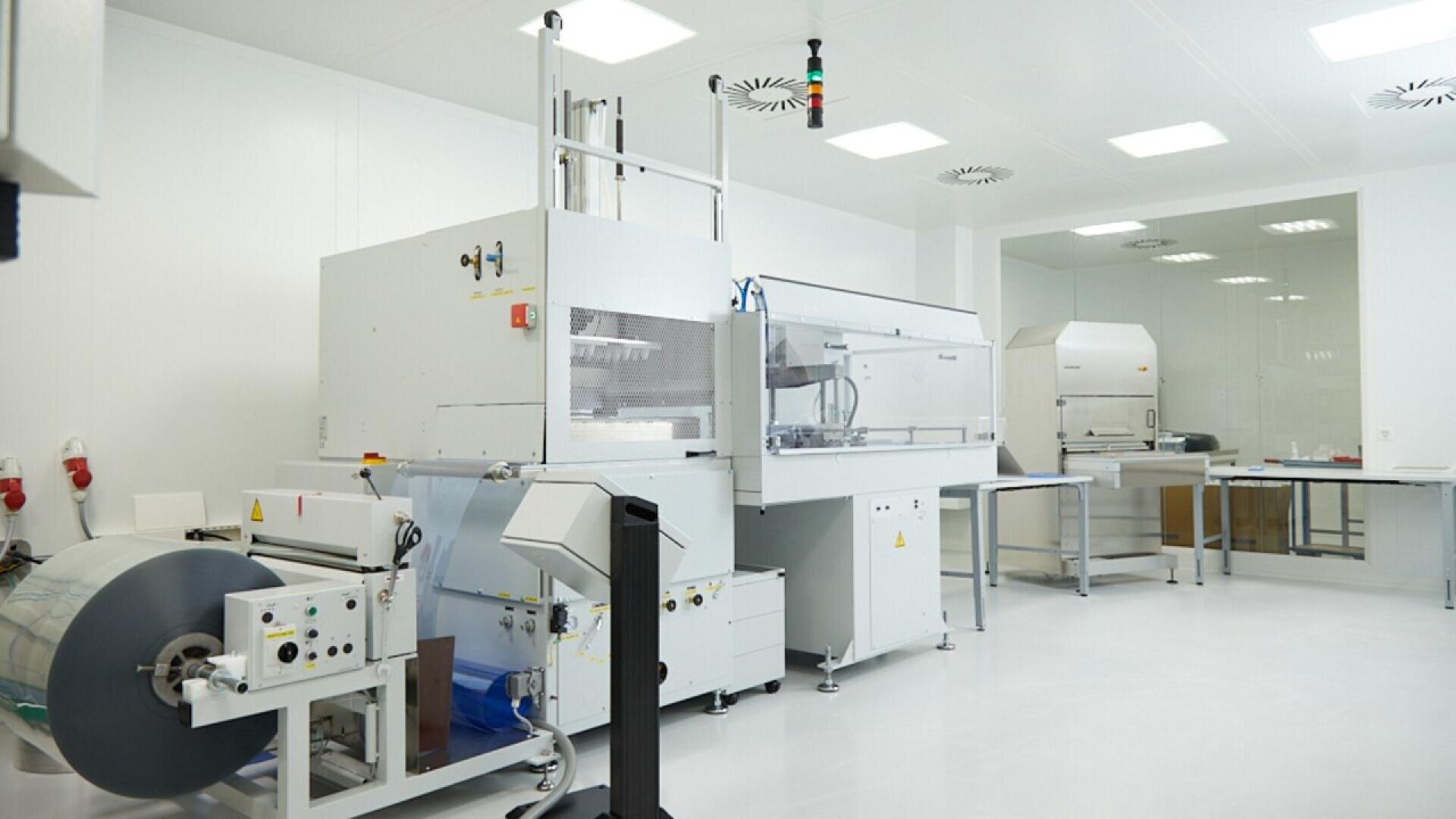 A clean and bright laboratory with advanced machinery, white walls, and ample lighting. Equipment and workstations are neatly arranged in a spacious, sterile environment.