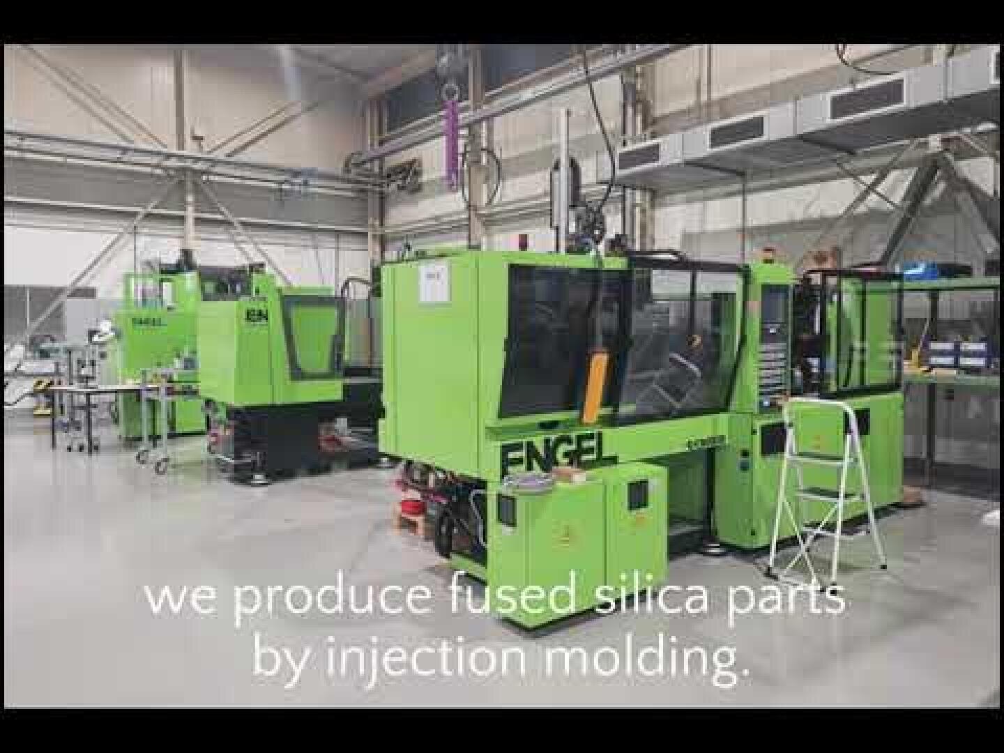 Two green ENGEL injection molding machines in a clean, modern factory environment. The text on the picture reads: We manufacture parts from quartz glass using the injection molding process.