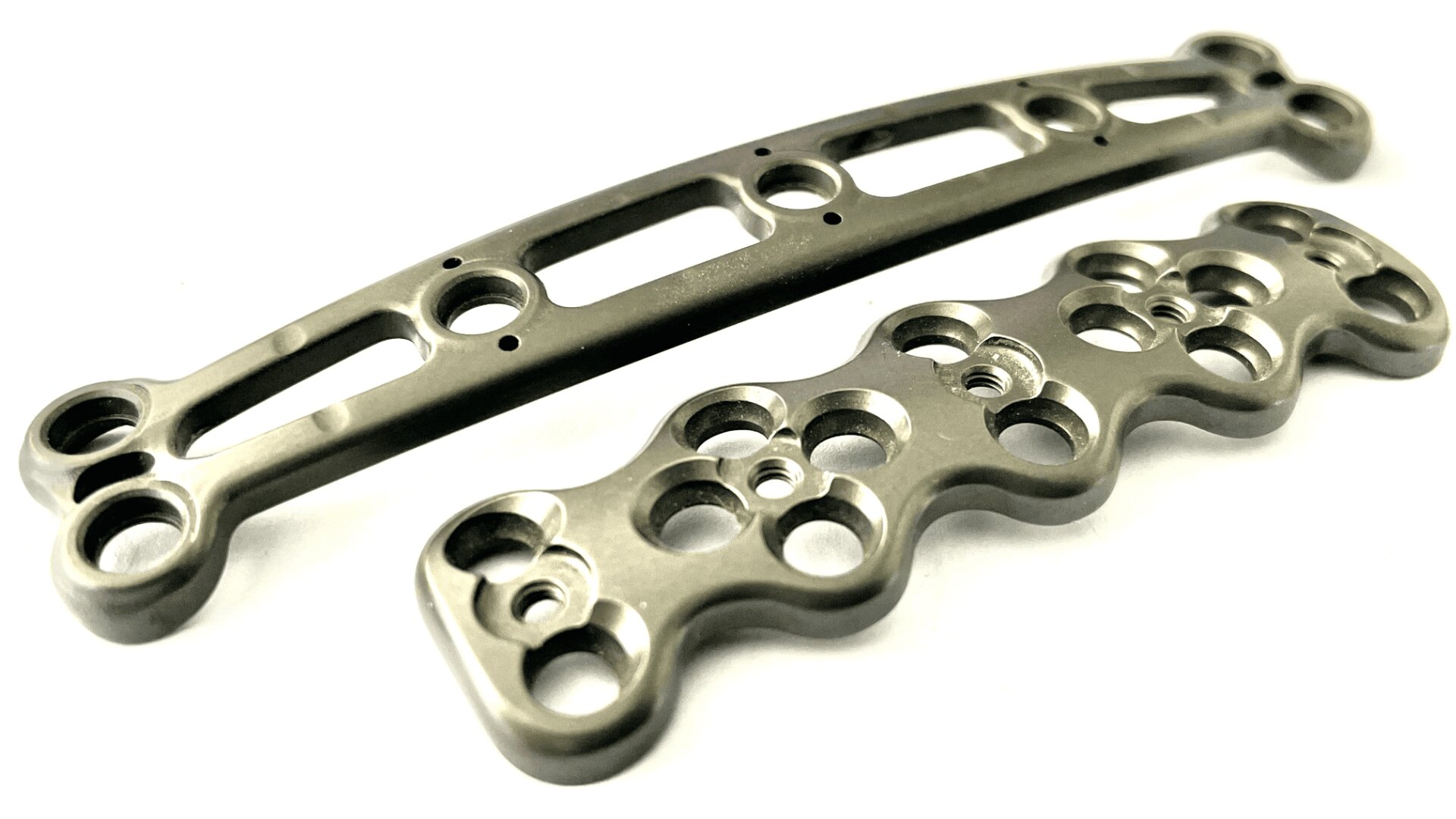 Zwei metallische orthopädische Knochenplatten mit mehreren Löchern und Konturen, die für die chirurgische Fixierung von Knochenbrüchen bestimmt sind, auf weißem Hintergrund.