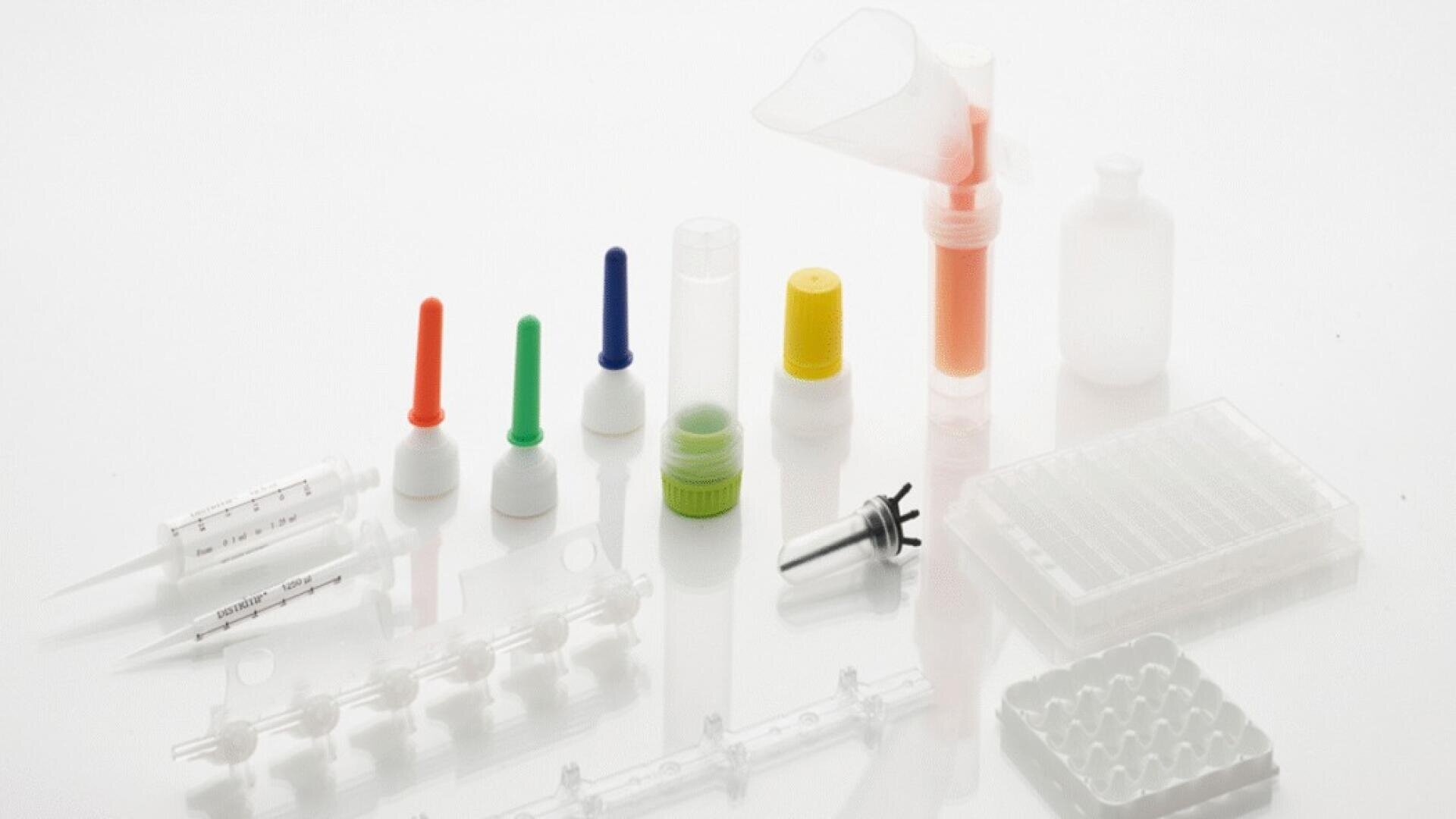 Various laboratory devices such as pipettes, closures, vials, a funnel, syringes, test tube racks, and containers are arranged on a white surface.